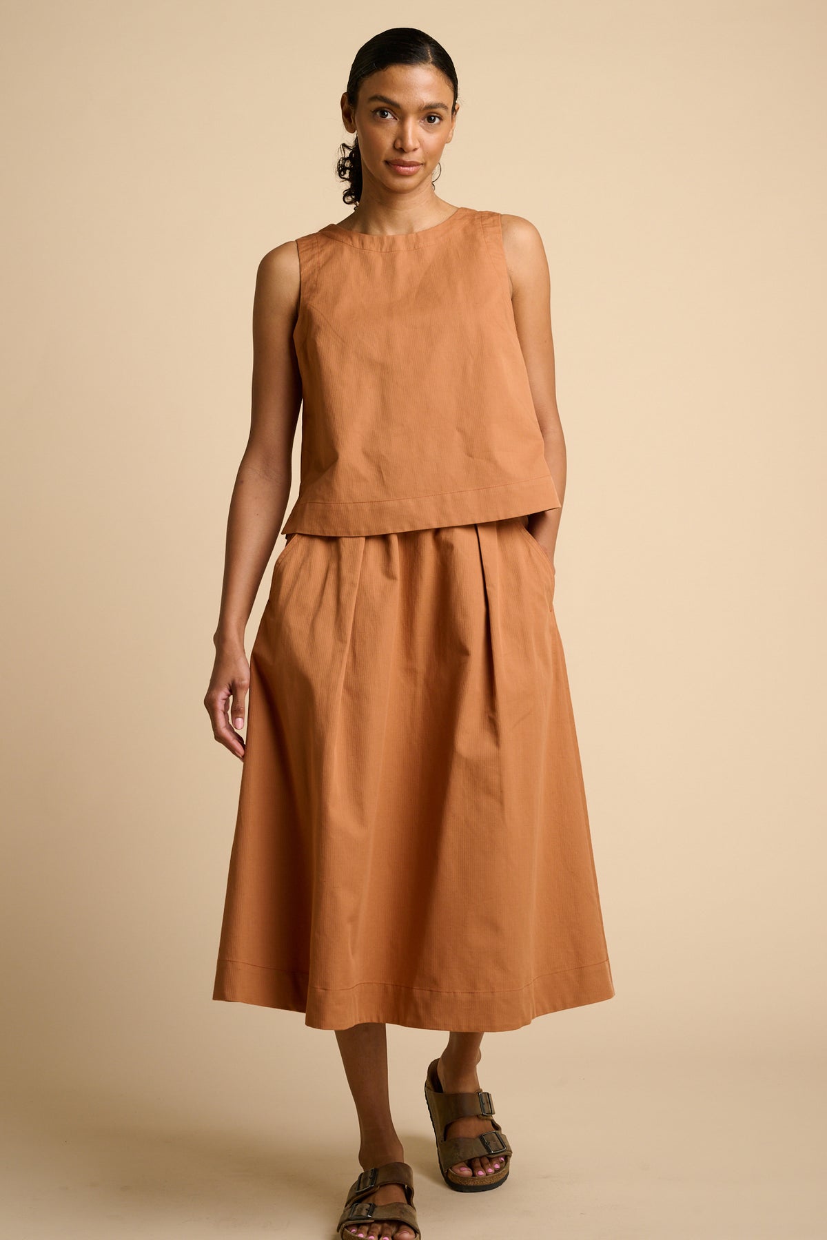 Woman wearing cinnamon top and skirt.