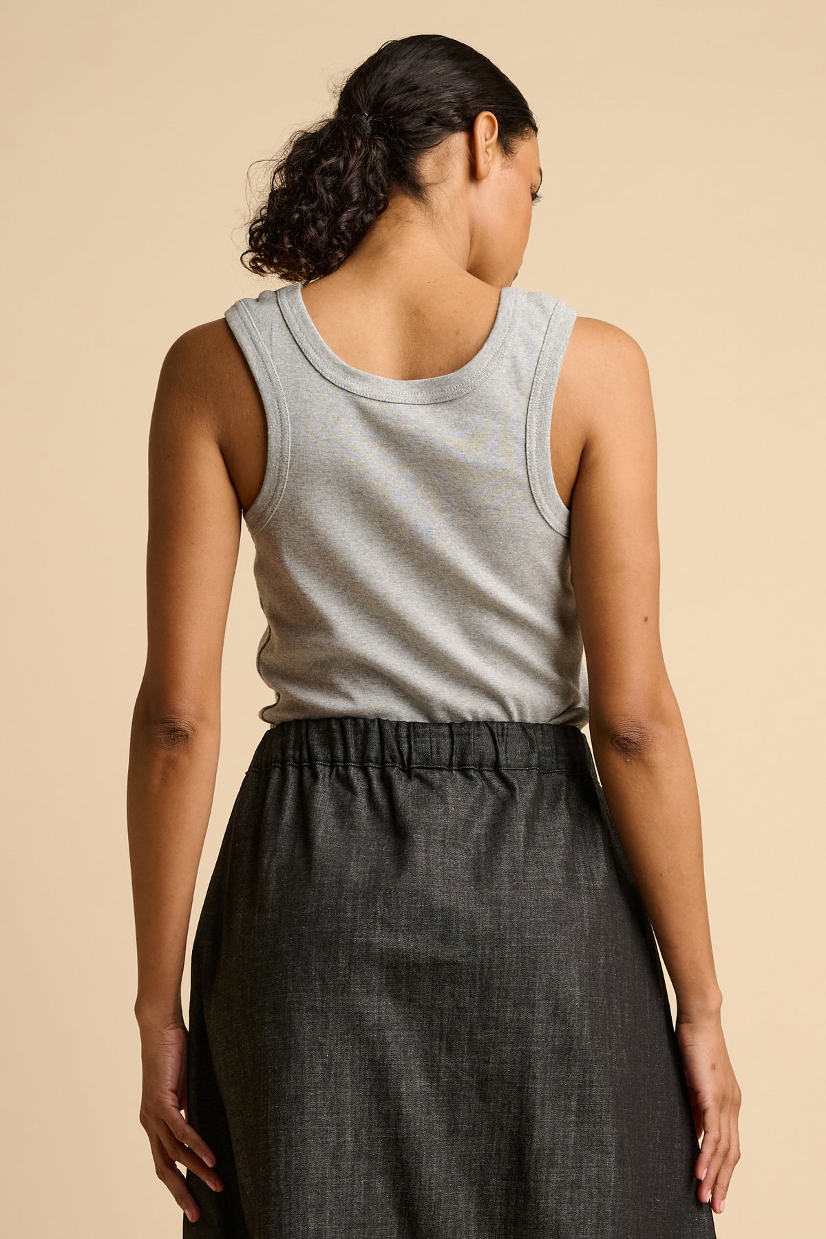 Woman wearing a grey tank top and black skirt on a beige background