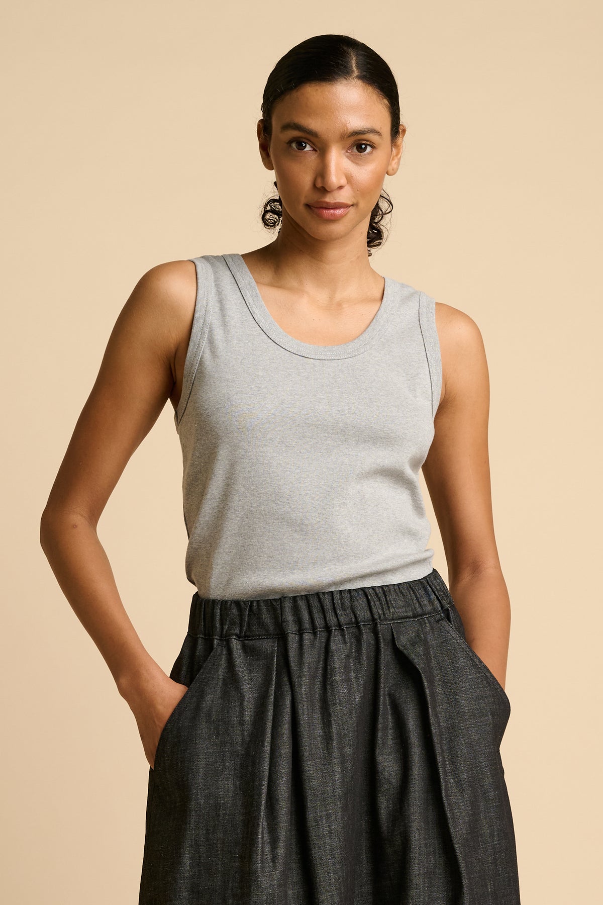 Woman wearing a grey tank top and black denim skirt against a beige background