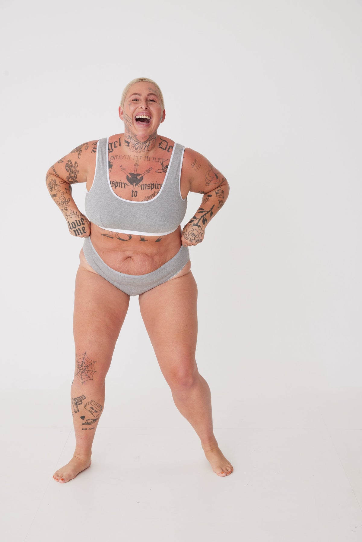 Cheerful, tattooed, white female wearing grey low rise brief