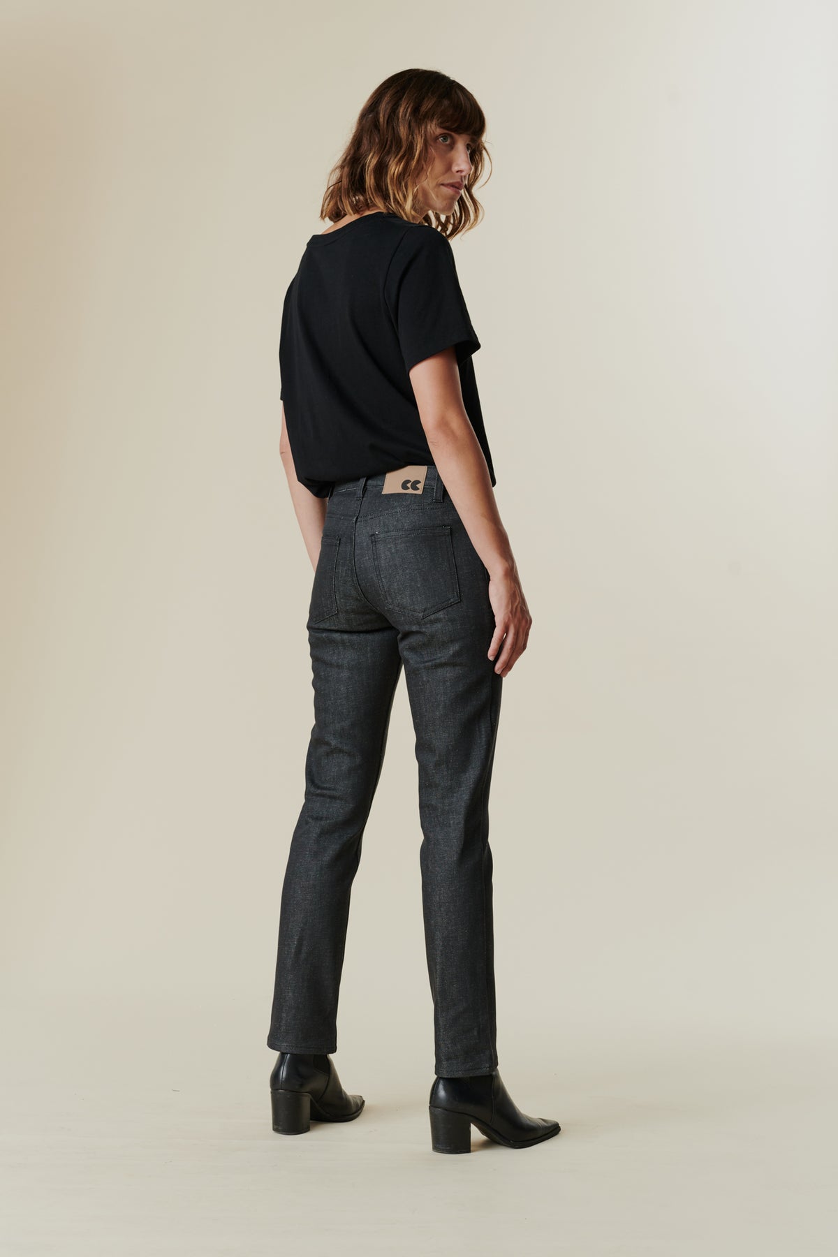 Full body image of back of female wearing mid rise straight leg jeans in black