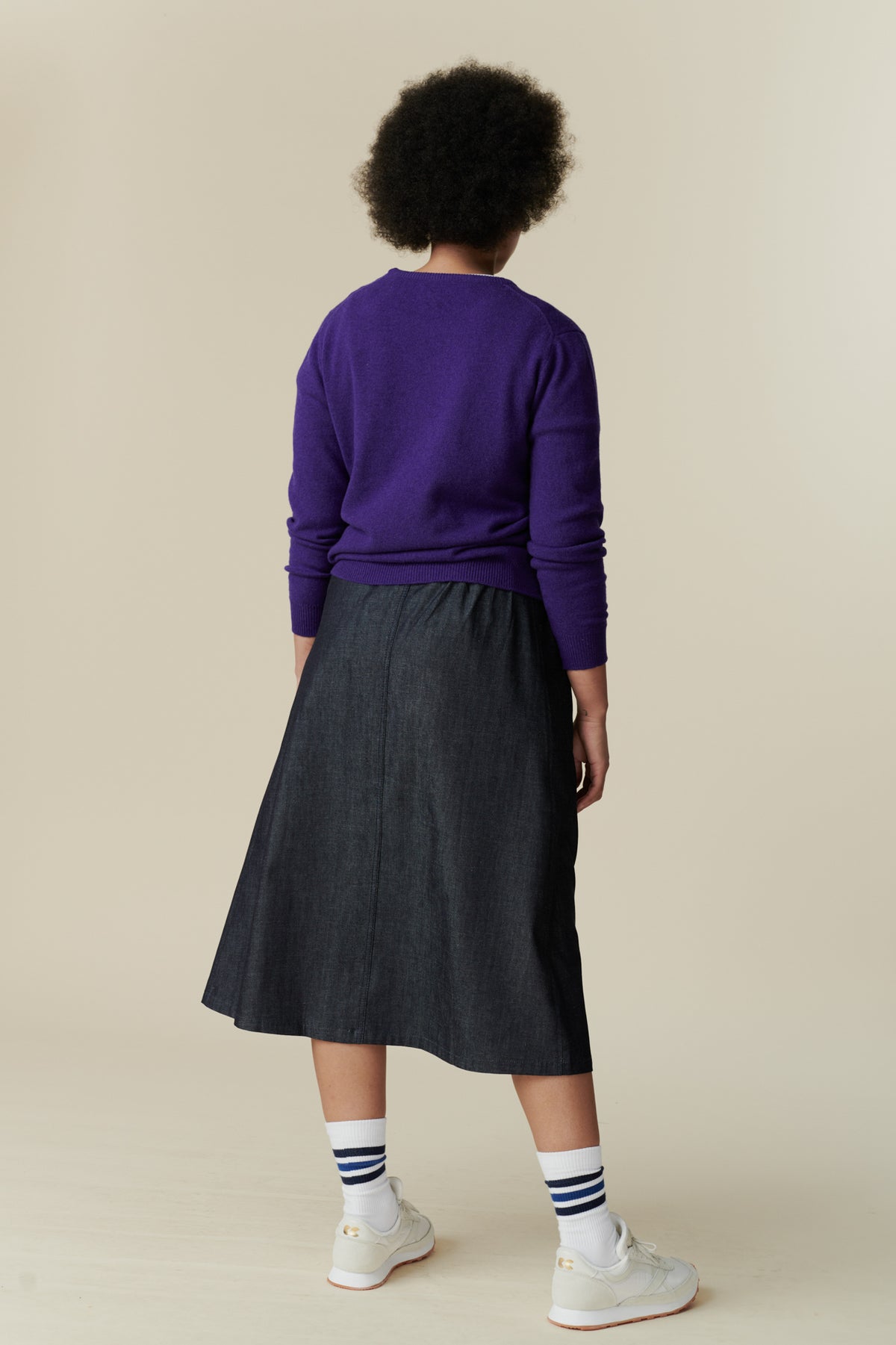 
            The back of female wearing midi skirt in denim paired with lambswool jumper in purple