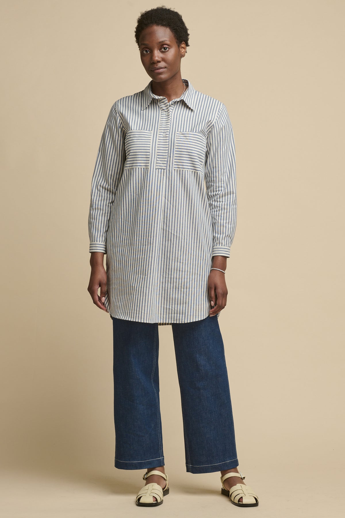 Full body image of black female wearing women's Olivia shirt dress in navy white stripe. Worn over blue work jeans