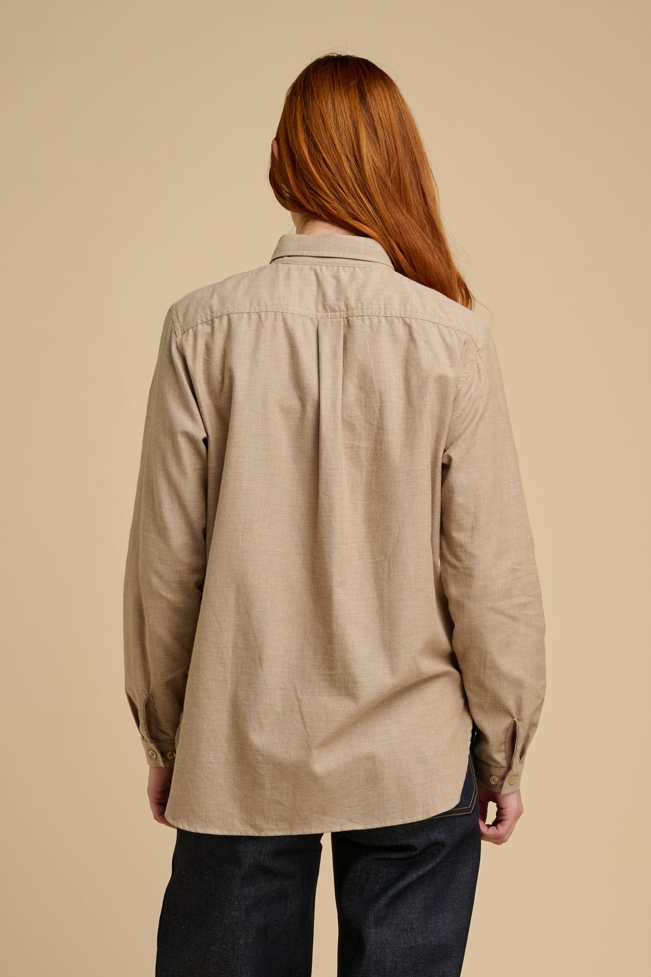 Woman wearing a beige shirt standing against a stone wall