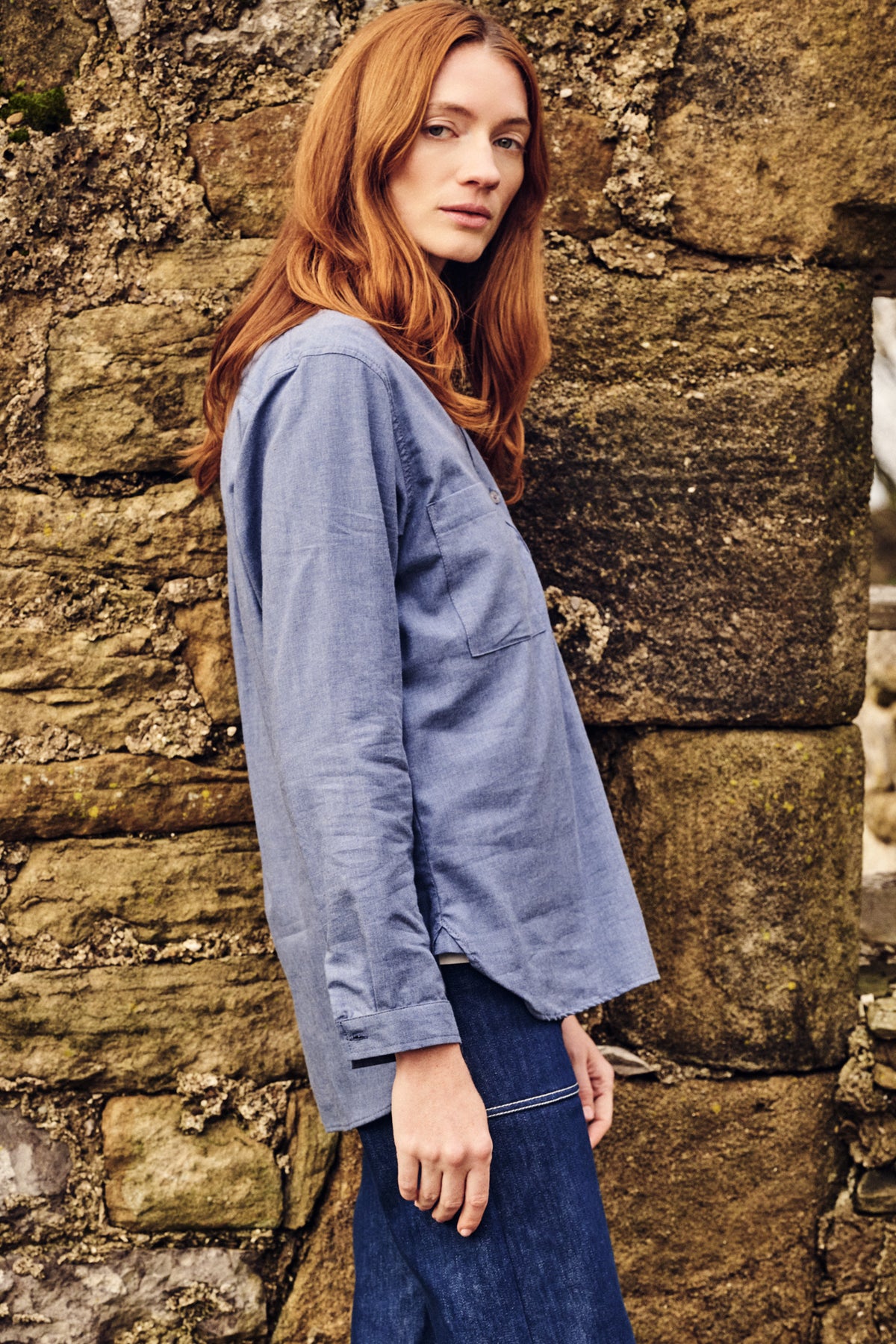 Woman wearing a blue jacket and jeans against a stone wall