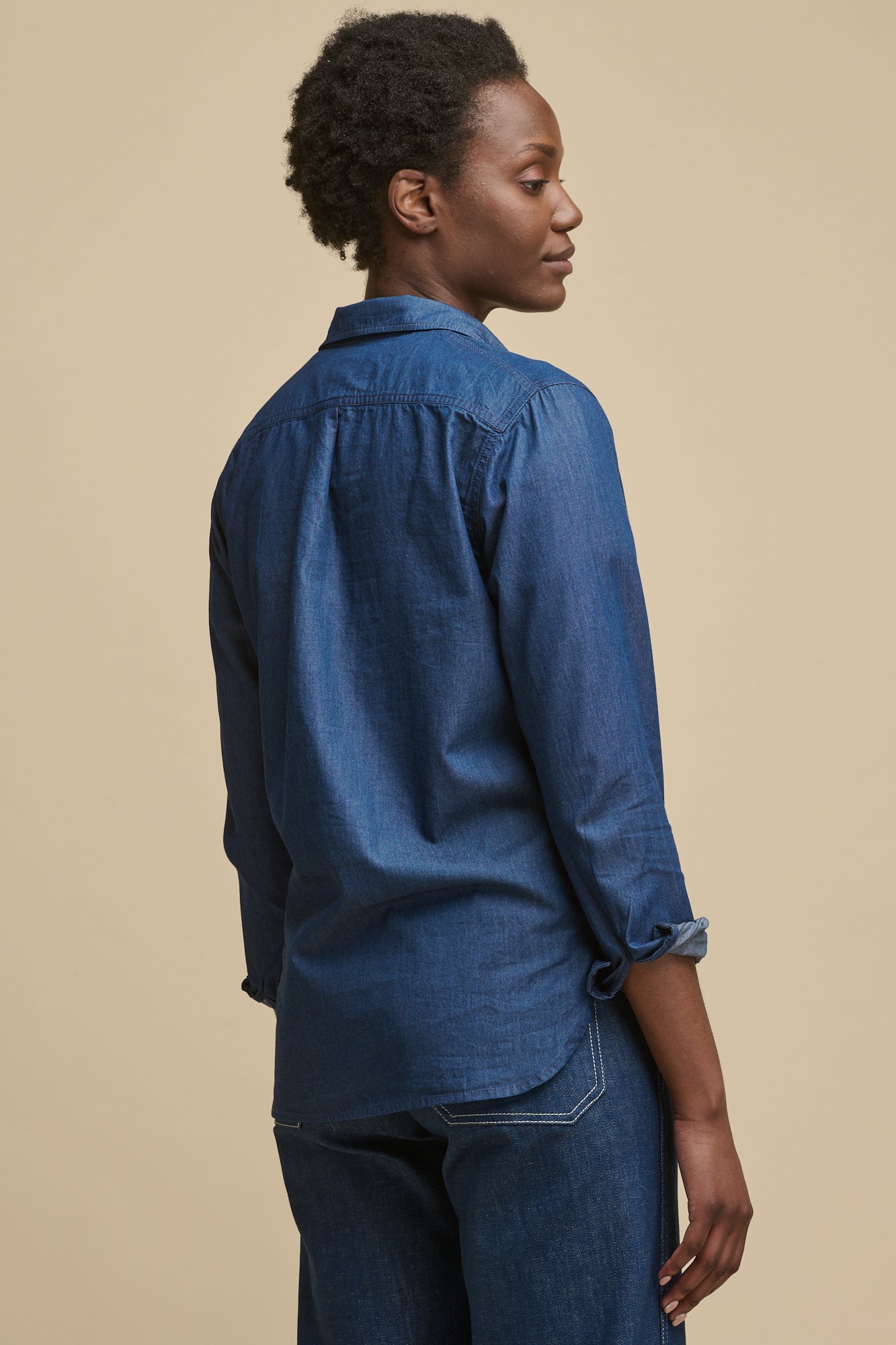 Thigh up image of female wearing Olivia half placket lightweight denim shirt in indigo with the sleeves rolled up slightly