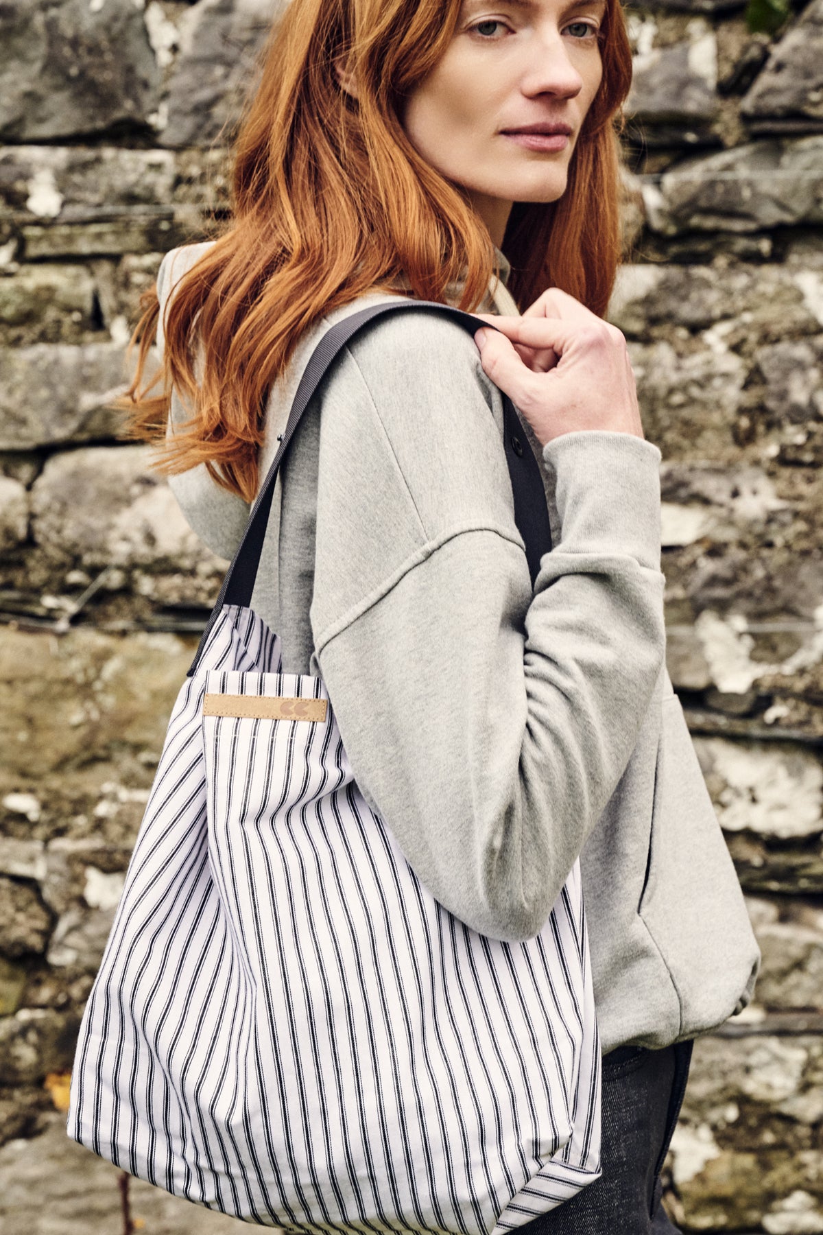 Woman carrying a striped bag against a stone wall