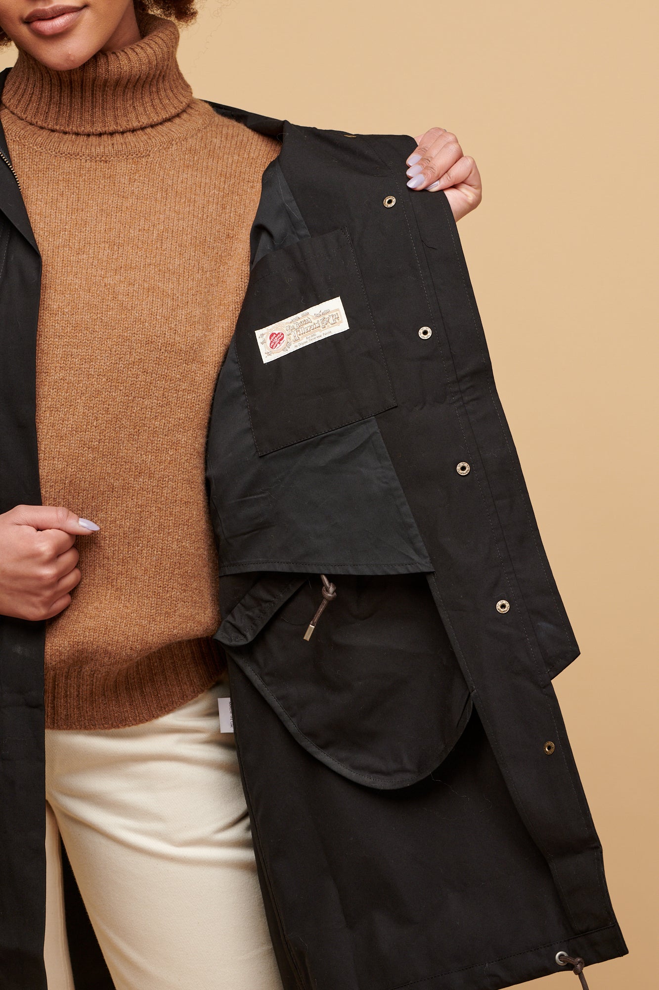 Female holding one side of the coat to show the inner lining and British Millerain label 