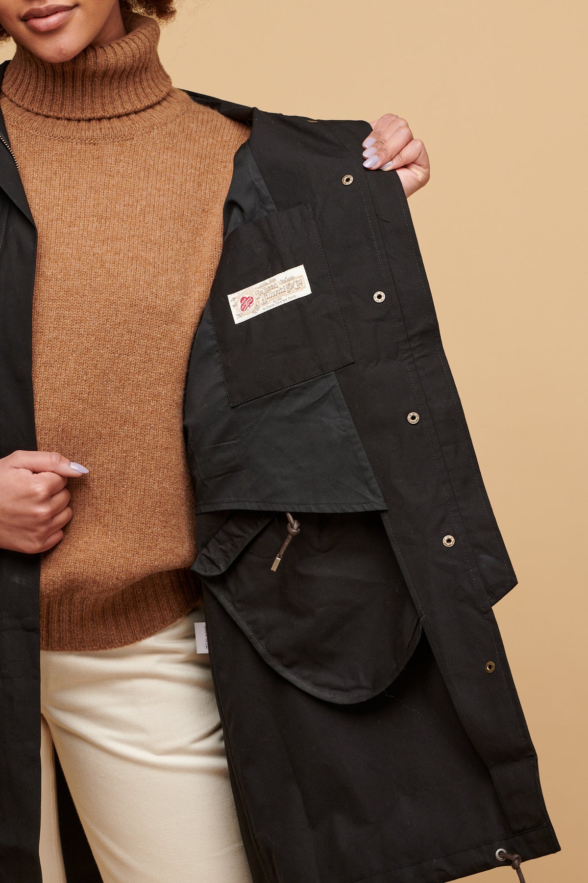 Female holding one side of the coat to show the inner lining and British Millerain label
