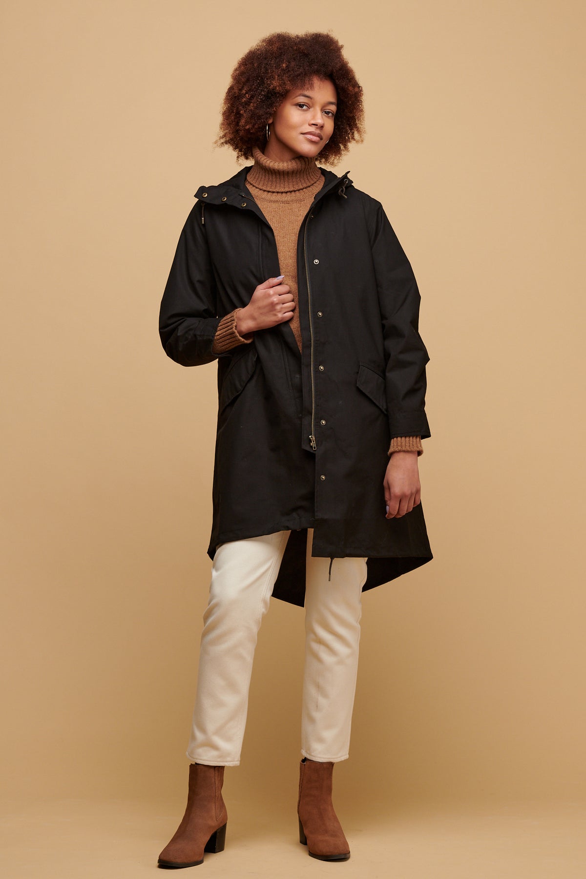 Female wearing women's parka coat in black worn unzipped over lambswool roll neck jumper in dark camel paired with gloria jean in ecru