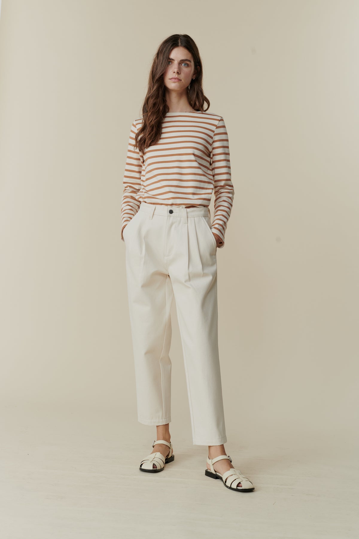 Full body front image of white female with long brunette hair wearing women's pleated jeans in ecru, paired with breton in ecru cinnamon