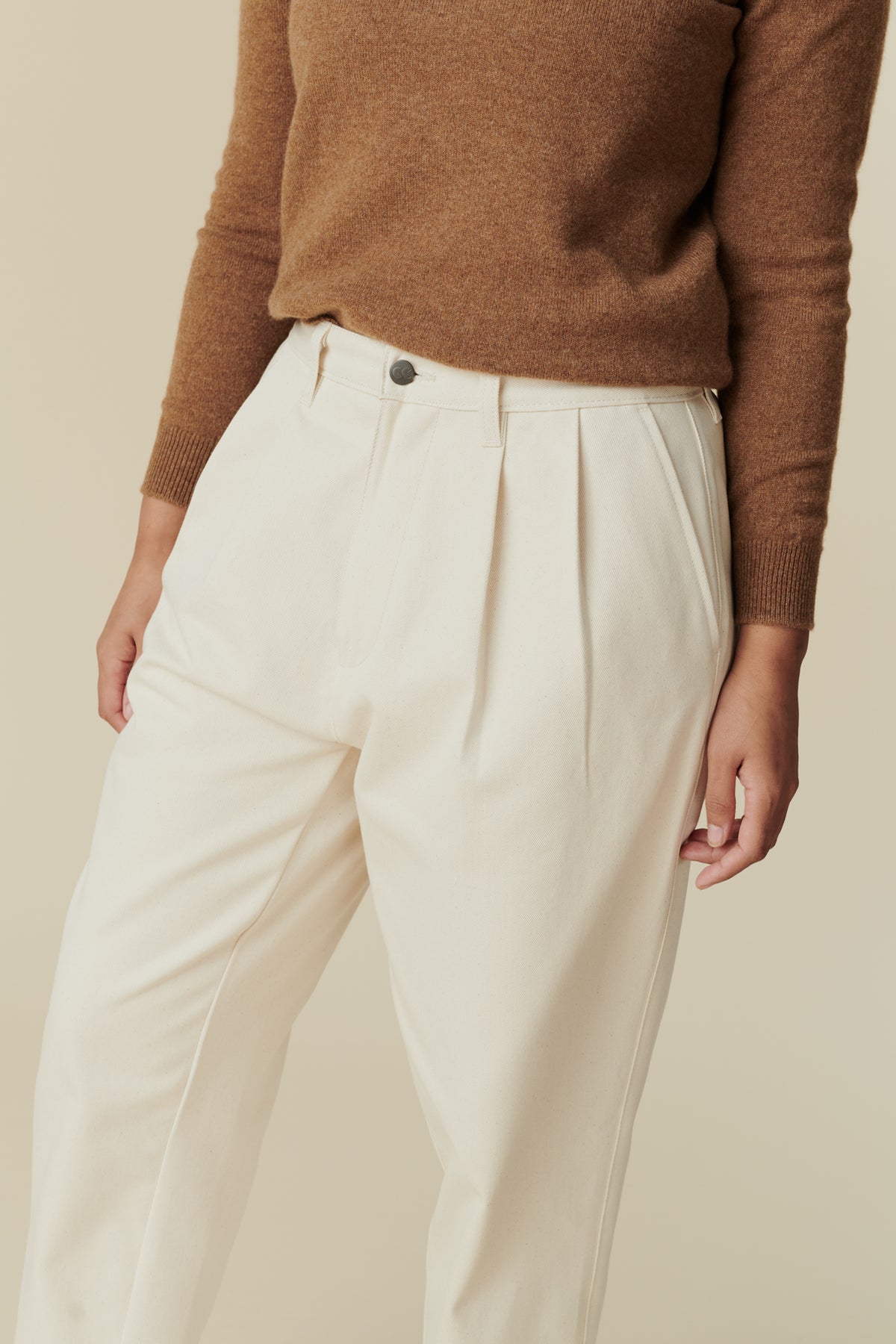 Detail shot of female wearing women's pleated jean in ecru paired with dark camel lambswool crew neck jumper