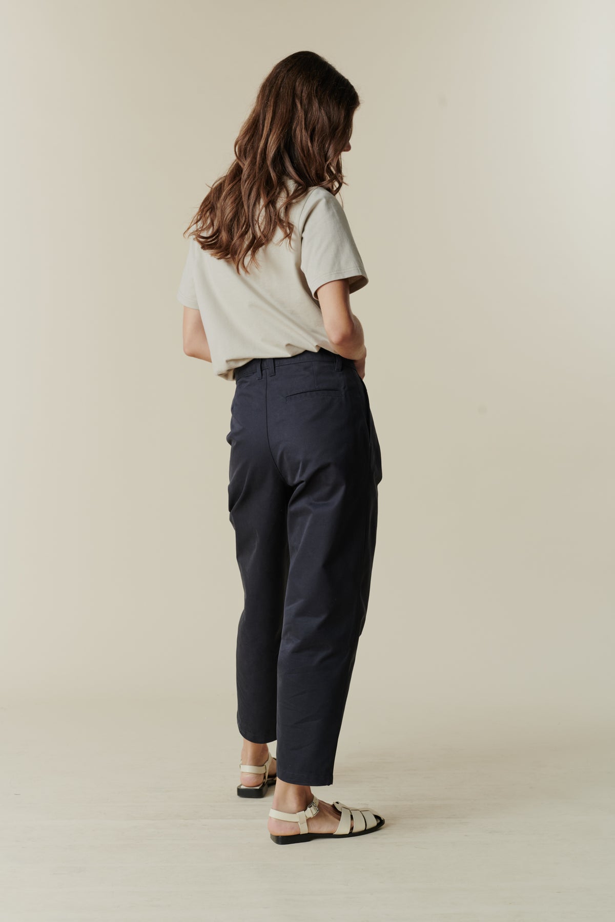 Full body image of back of female wearing pleated jeans in navy