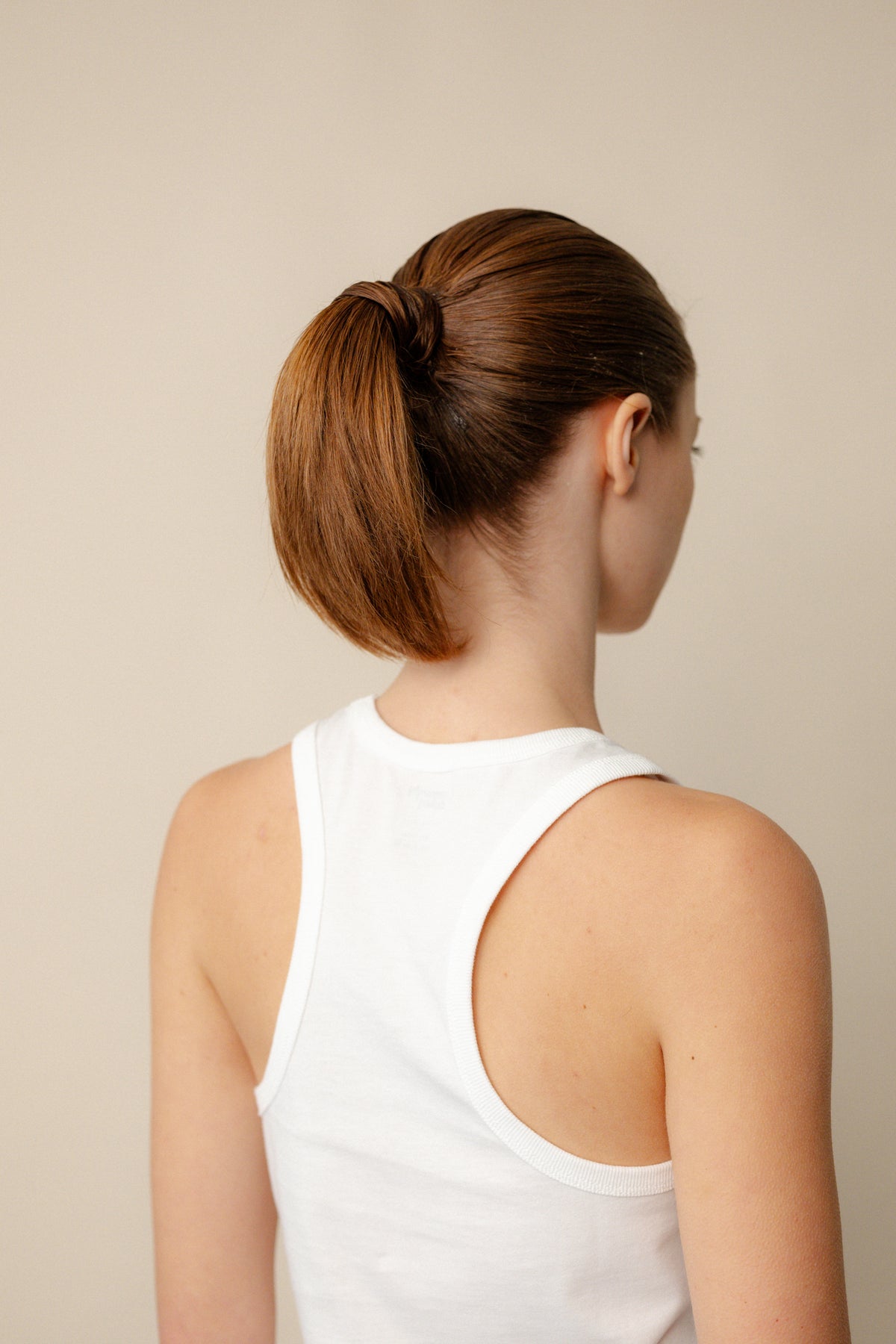 
            Back of brunette female with hair in ponytail showing racer back vest in white