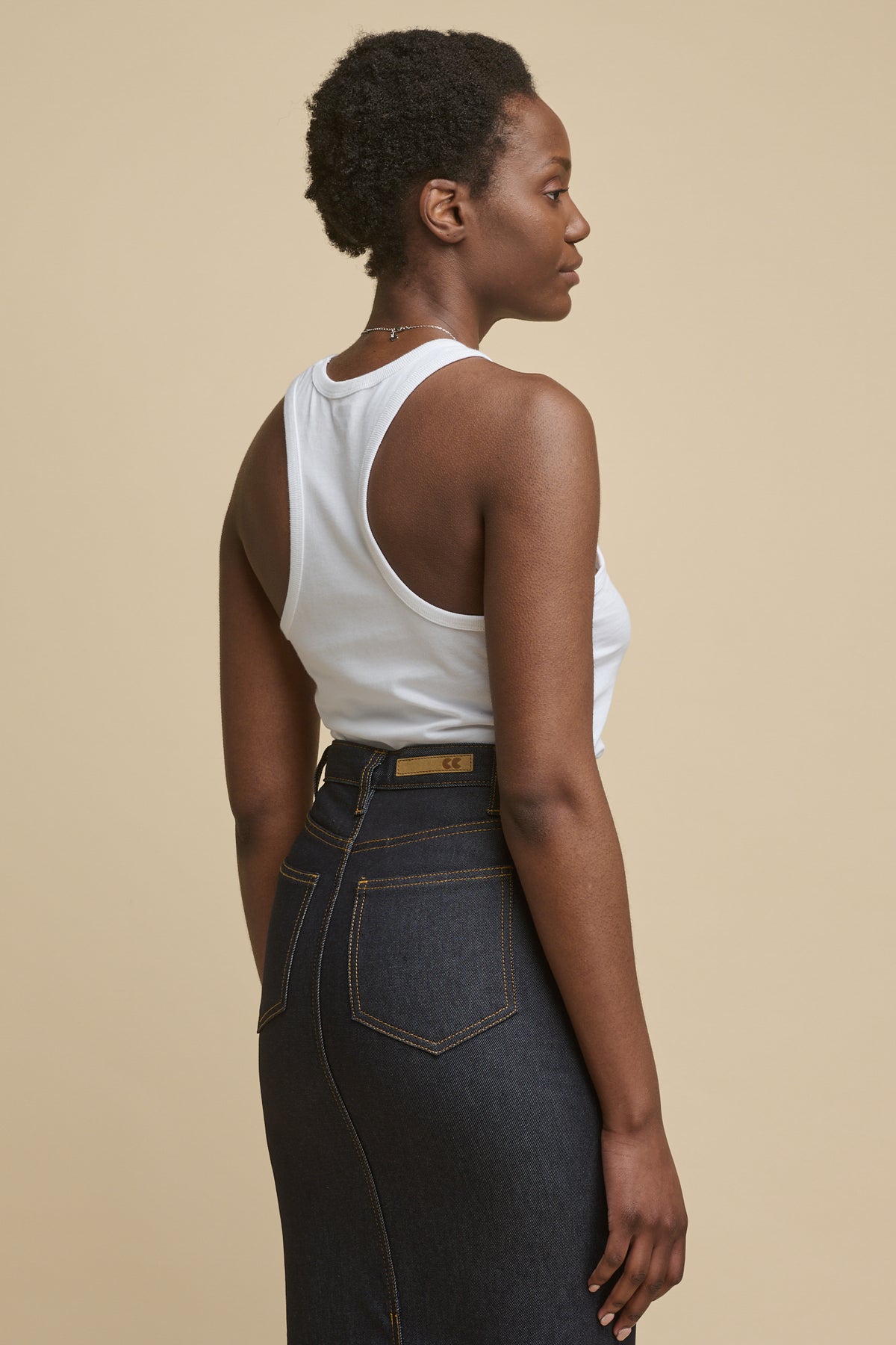 Thigh up image of the back of female wearing racer back vest in white paired with Frankie denim maxi skirt in indigo