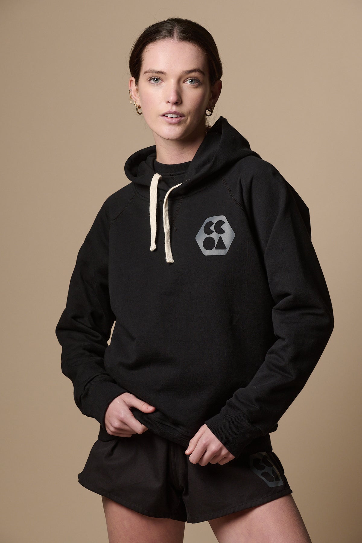 Thigh up image of the front of female wearing raglan hooded sweatshirt plastic free in black