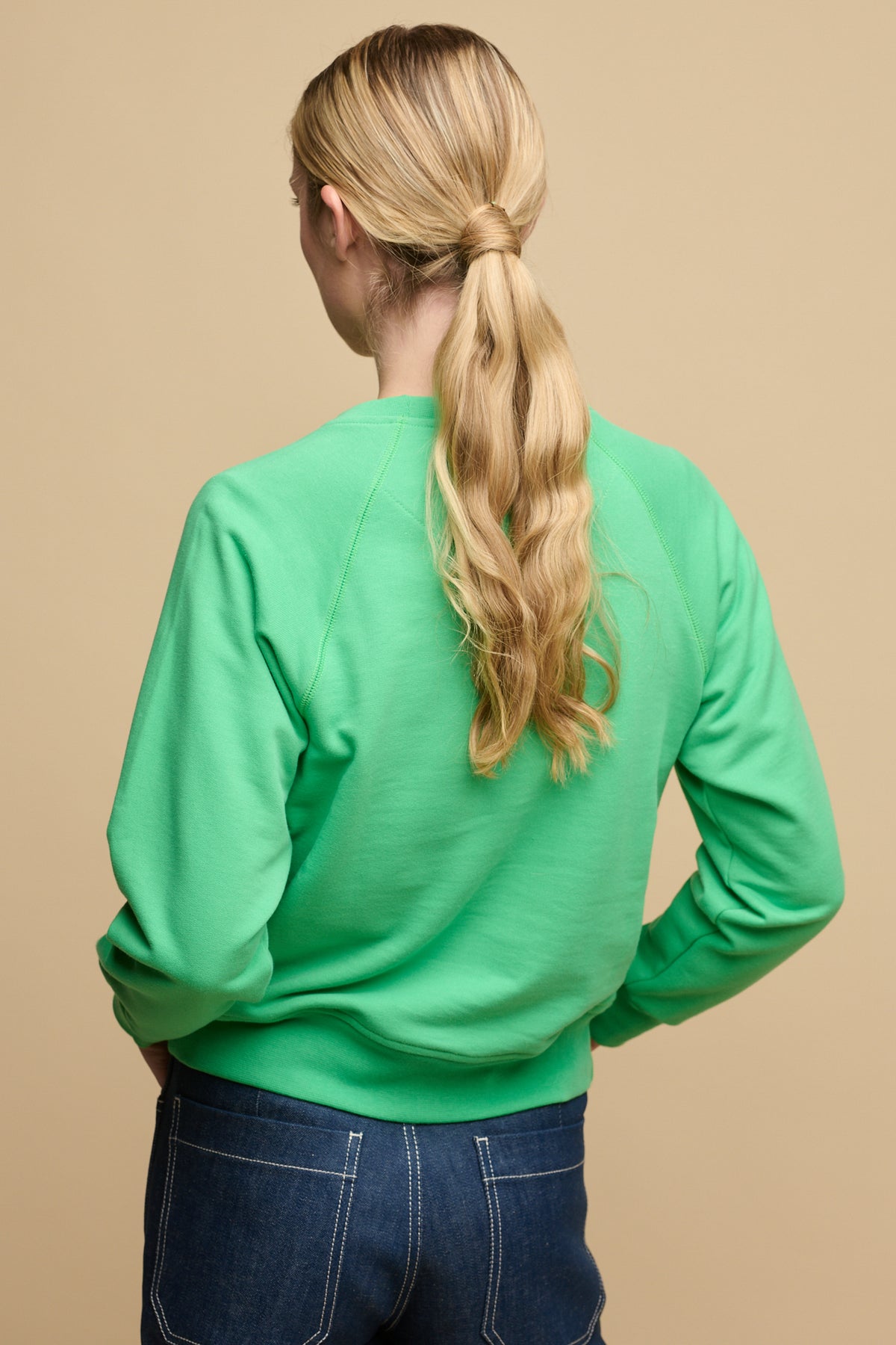 The back of female with long blonde hair tied back into low ponytail wearing raglan sweatshirt in apple green