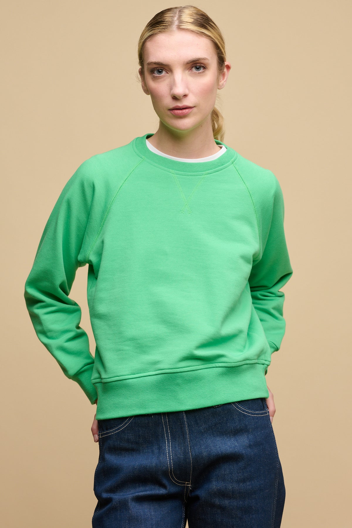 Female wearing raglan sweatshirt in apple green with hands on back of hips, sweatshirt worn over crew neck t shirt in white