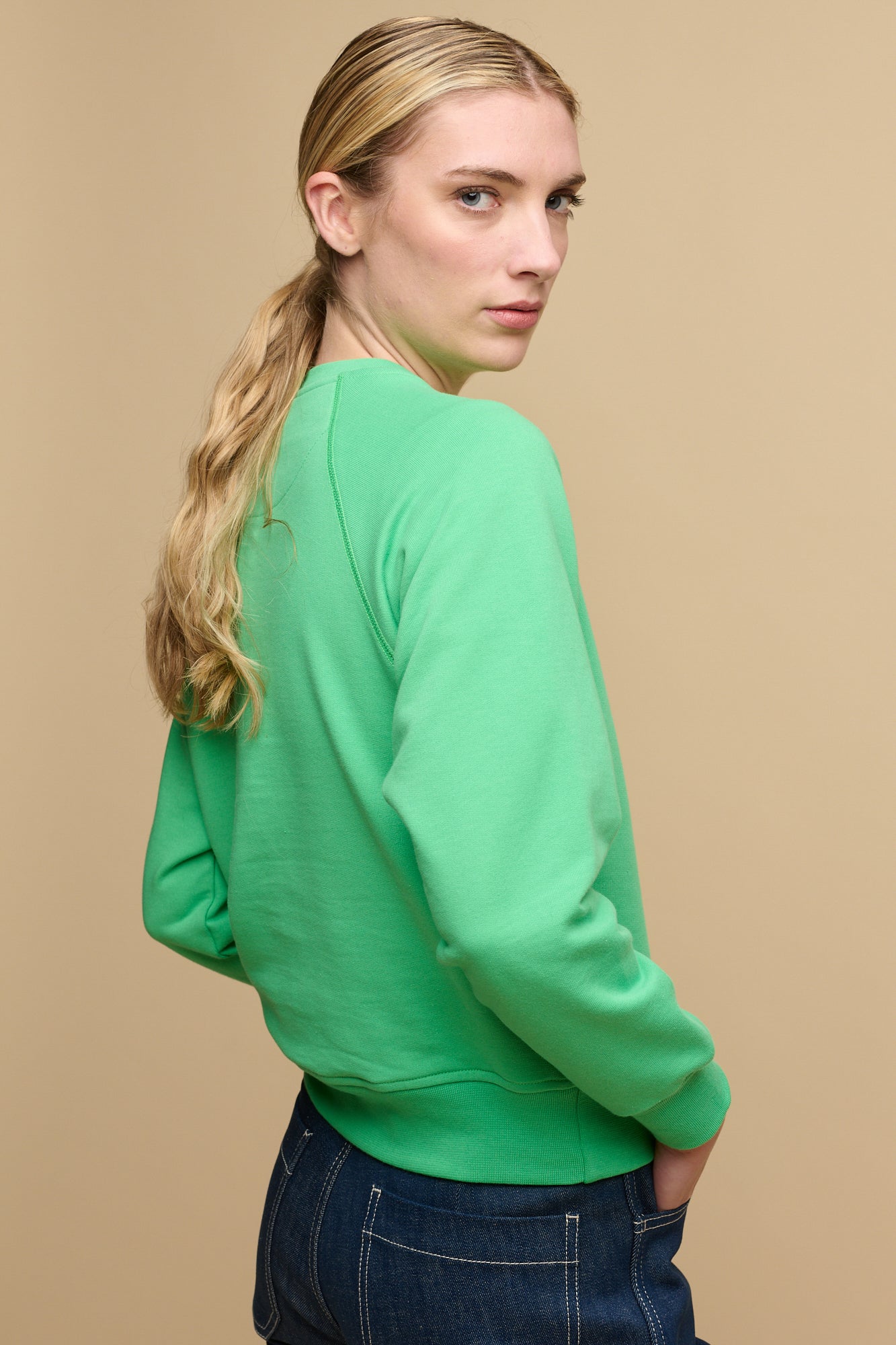 Hip up image of the side of female wearing raglan sweatshirt in apple green