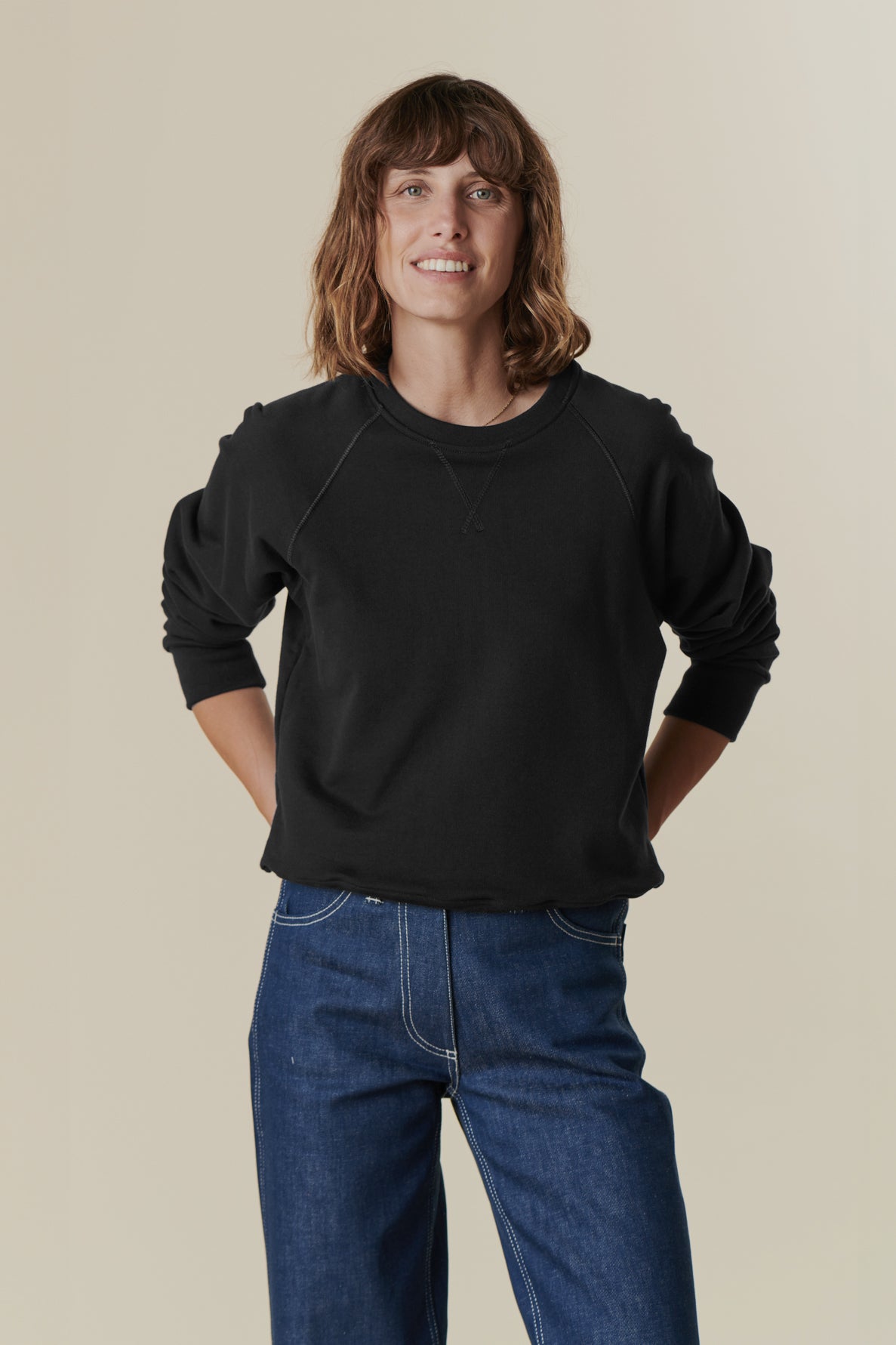 Thigh up front image of brunette female wearing black raglan sweatshirt