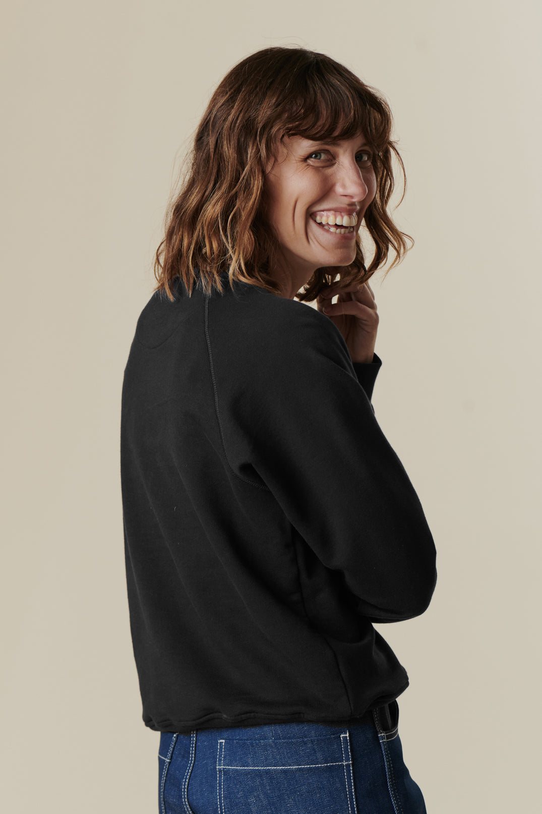 Image of brunette female from behind looking back to the camera, wearing black raglan sweatshirt
