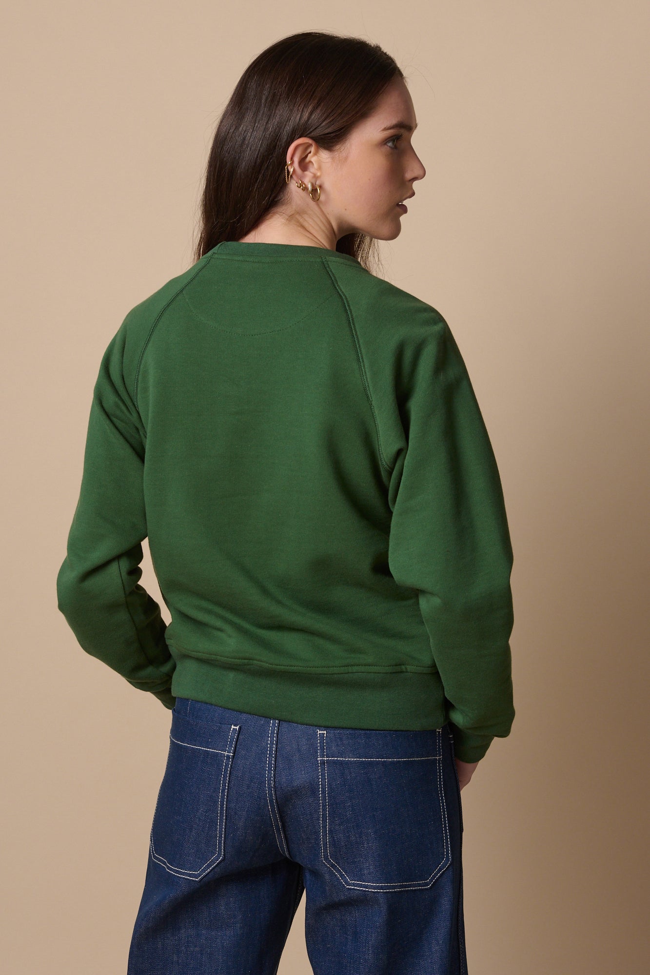 Thigh up image of female wearing raglan sweatshirt in bottle green