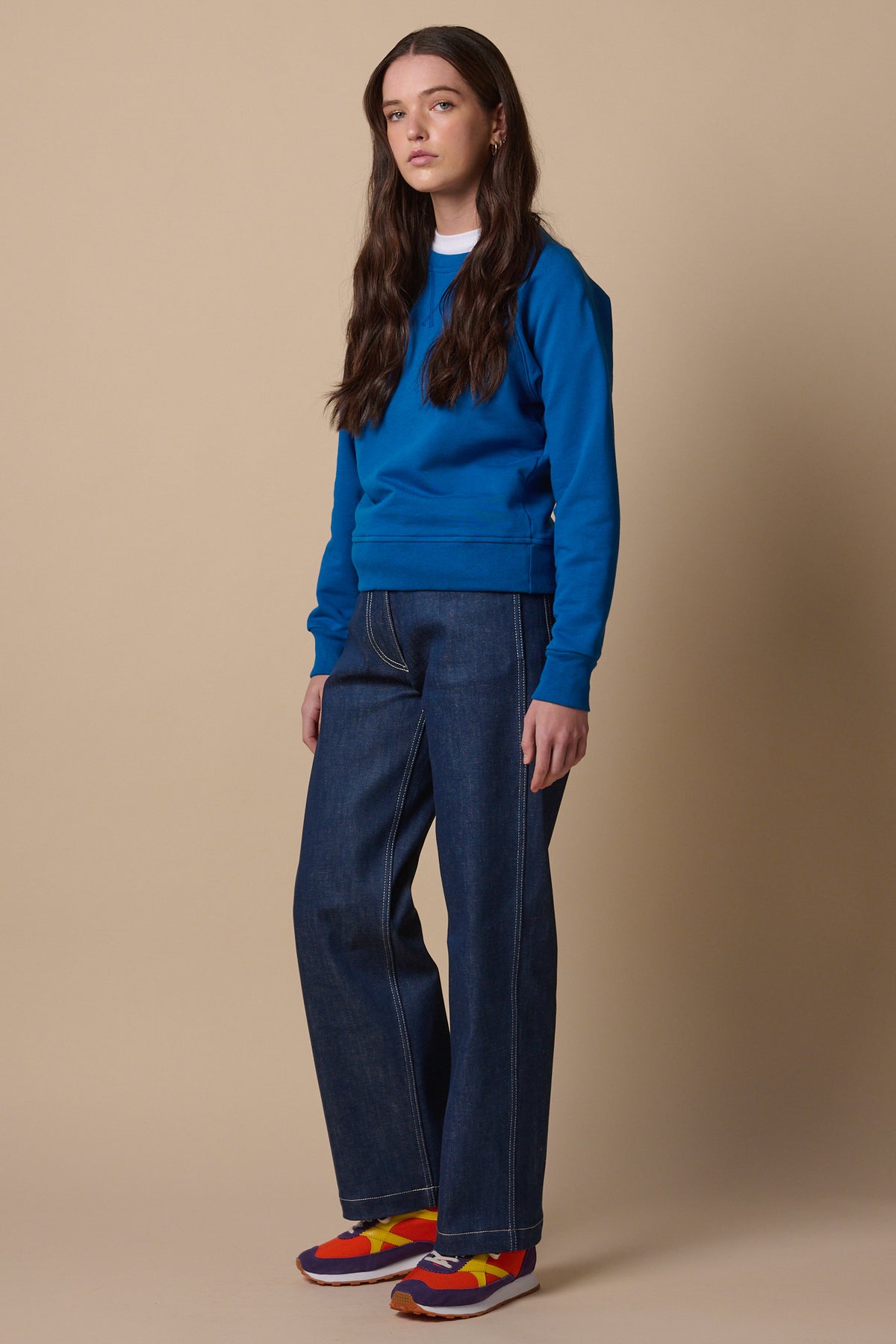 Full body image of female wearing raglan sweatshirt in cobalt paired with work jeans in blue