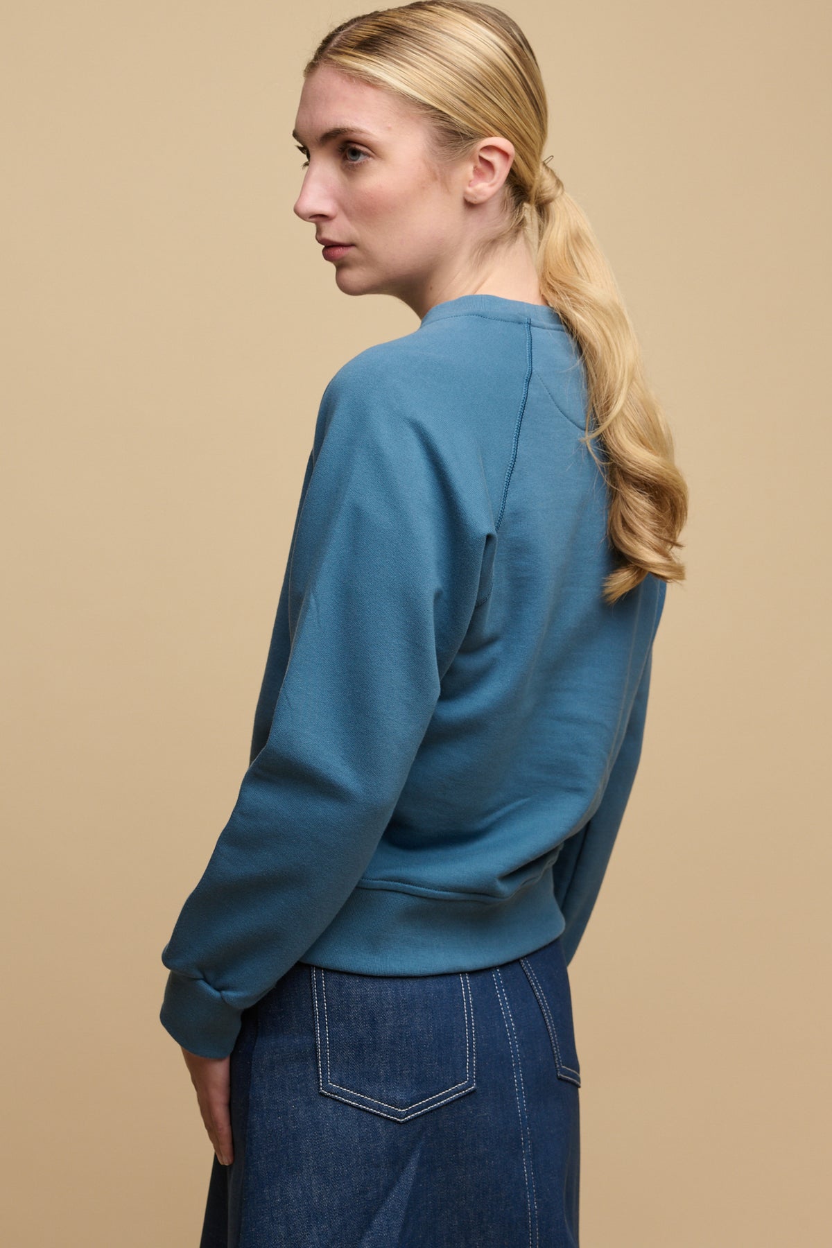 Back of female with long blonde hair tied back into low ponytail wearing raglan sweatshirt in RAF blue