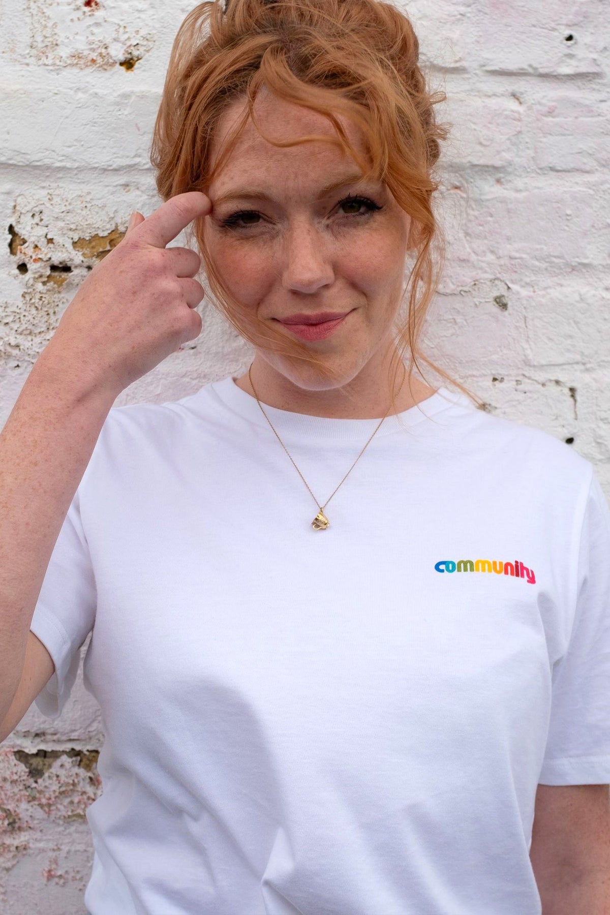 
            Actress Charlotte Spencer wearing a Short Sleeve white T-Shirt with branding on the chest, stood against a white brick wall