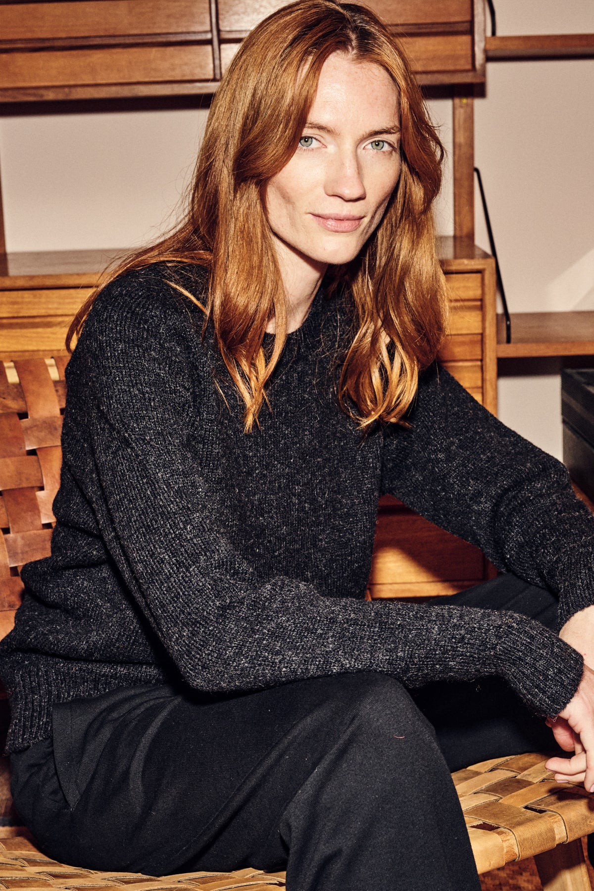 Woman wearing a charcoal shetland jumper sitting on a wooden bench indoors.