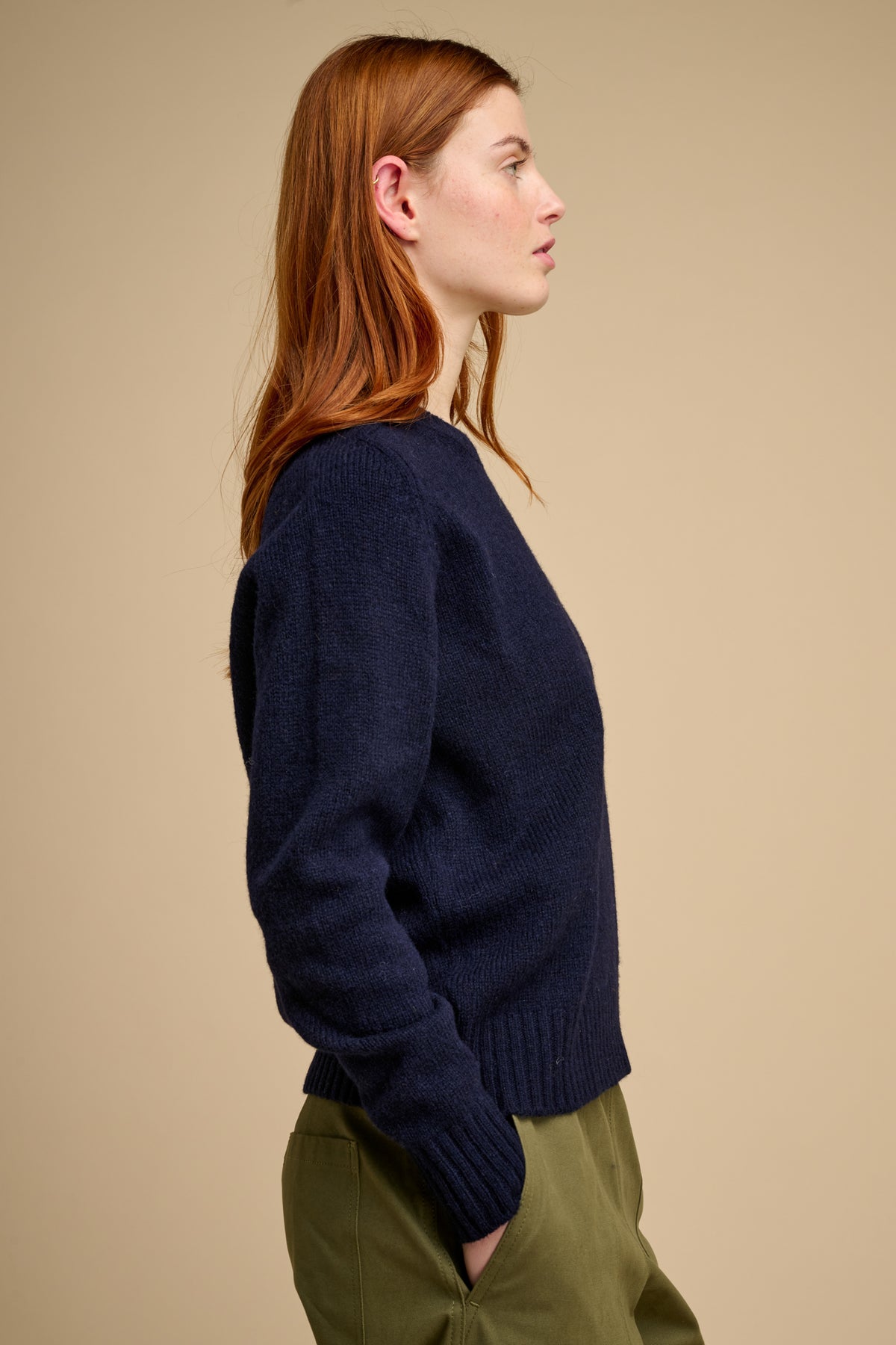 Woman wearing a navy sweater and green pants against a beige background