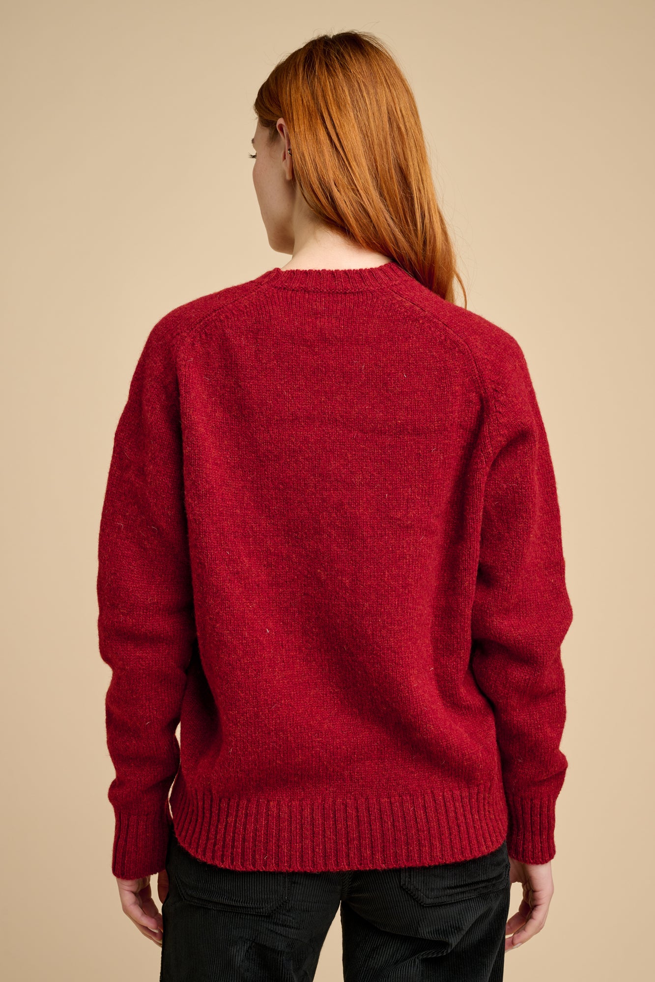 The back of a woman wearing a red sweater on a beige background