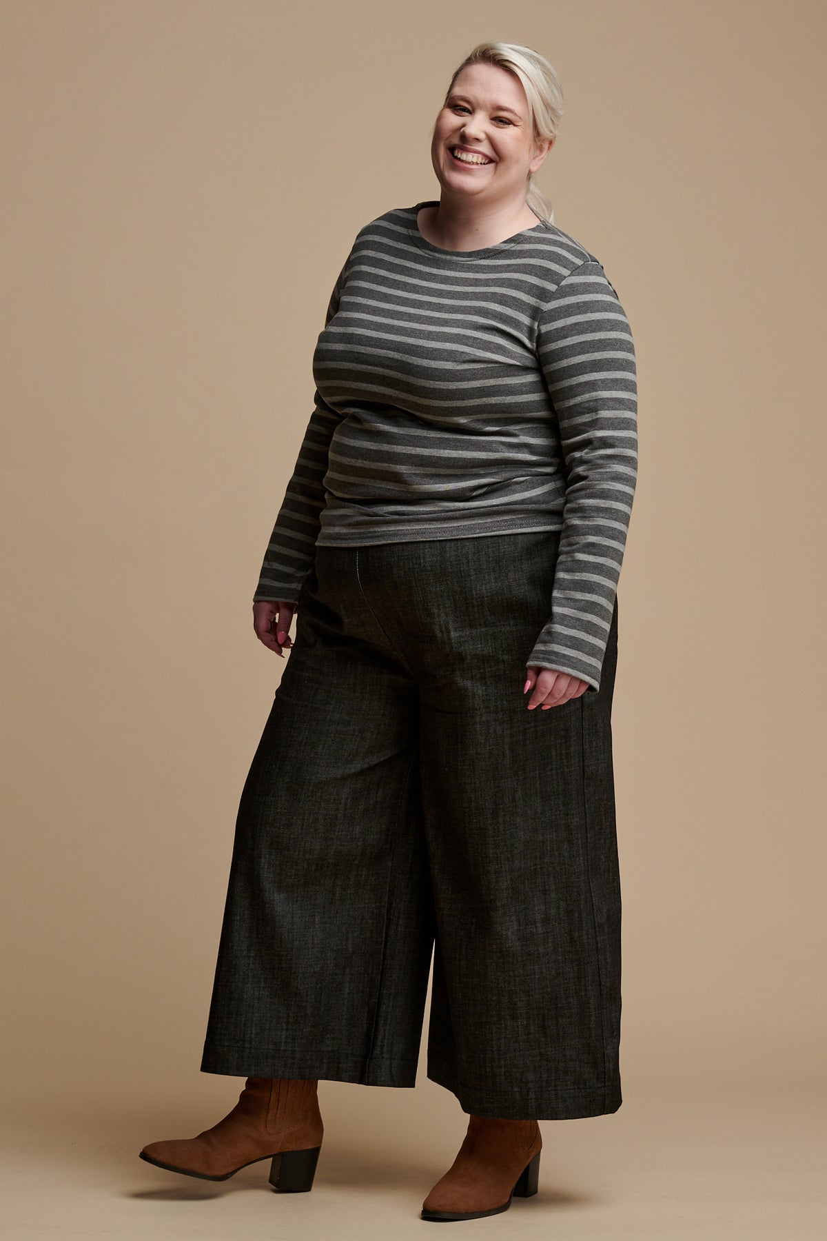 Smiley female wearing short PJ trousers in black denim paired with long sleeve Breton top in grey and charcoal stripe.