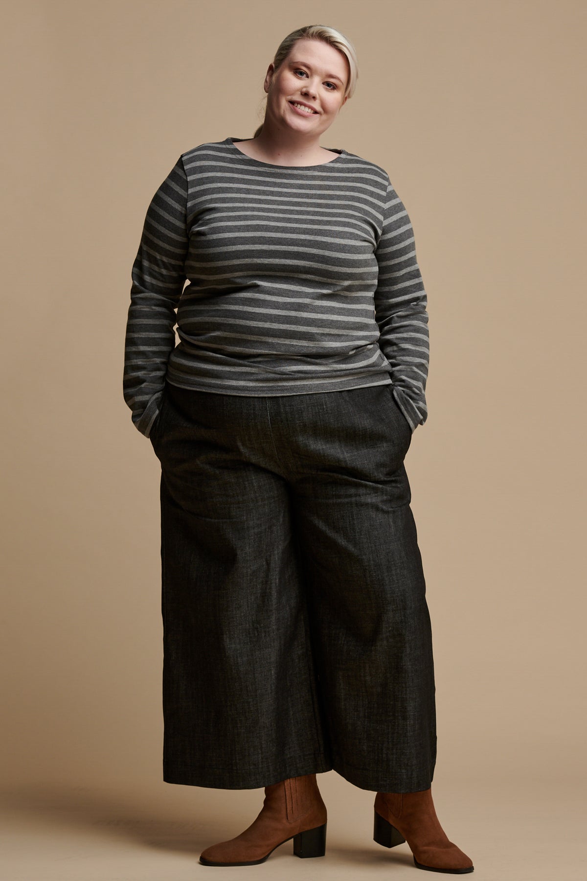 Smiley female wearing long sleeve Breton top in grey and charcoal marl stripe paired with short pj trousers in black denim and a brown suede boot