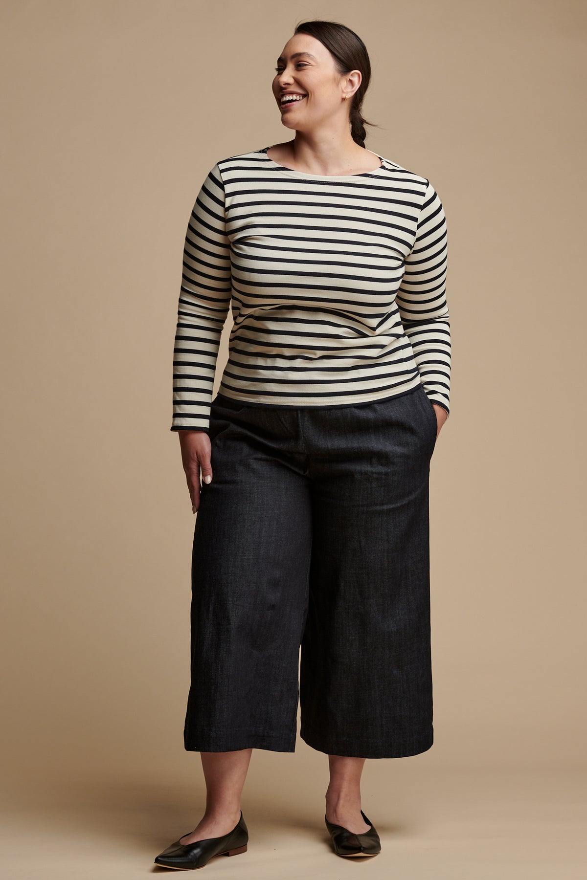 Smiley female with brown hair tied back wearing short pj pants in indigo denim paired with a long sleeve Breton top in ecru and navy stripe.