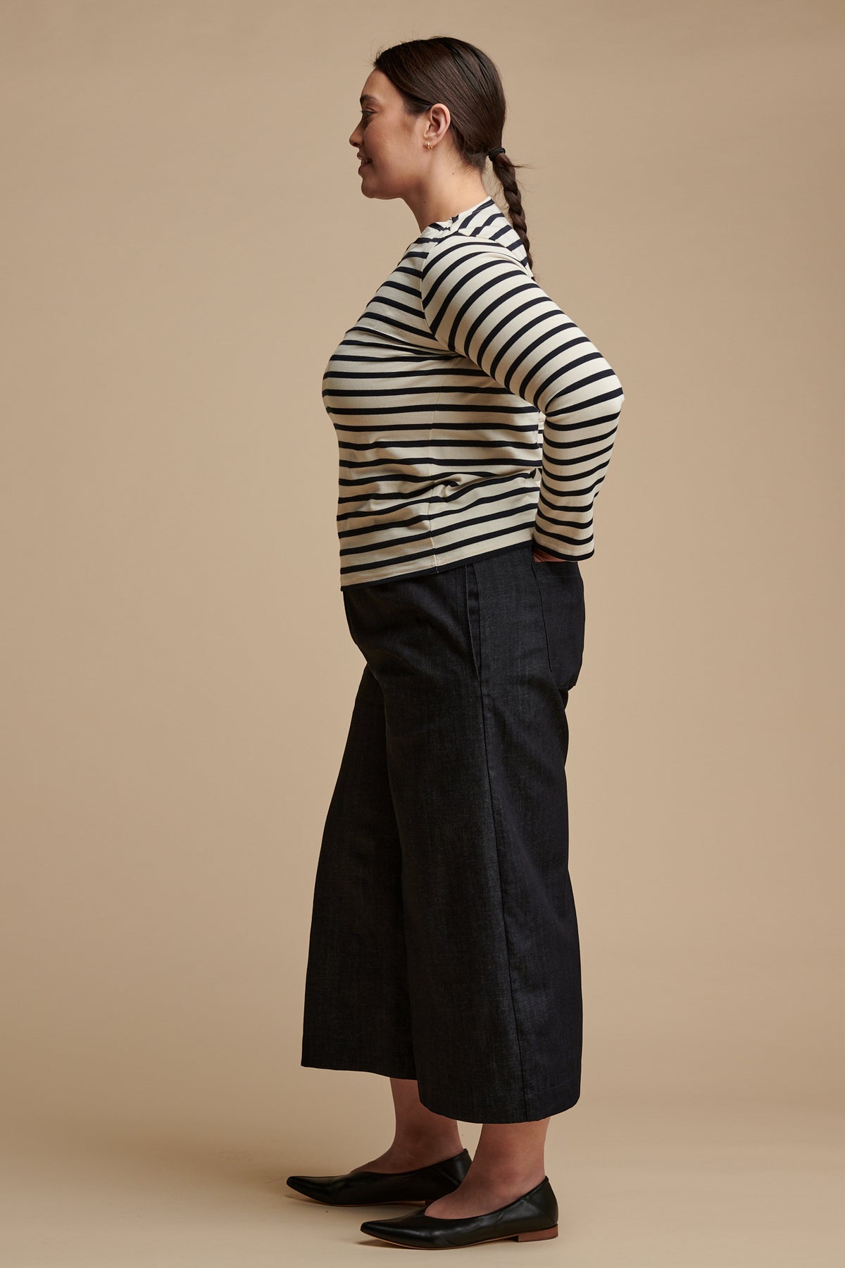 The side of female with brown hair tied back into a plait wearing long sleeve Breton top paired with short pj trousers in indigo denim.