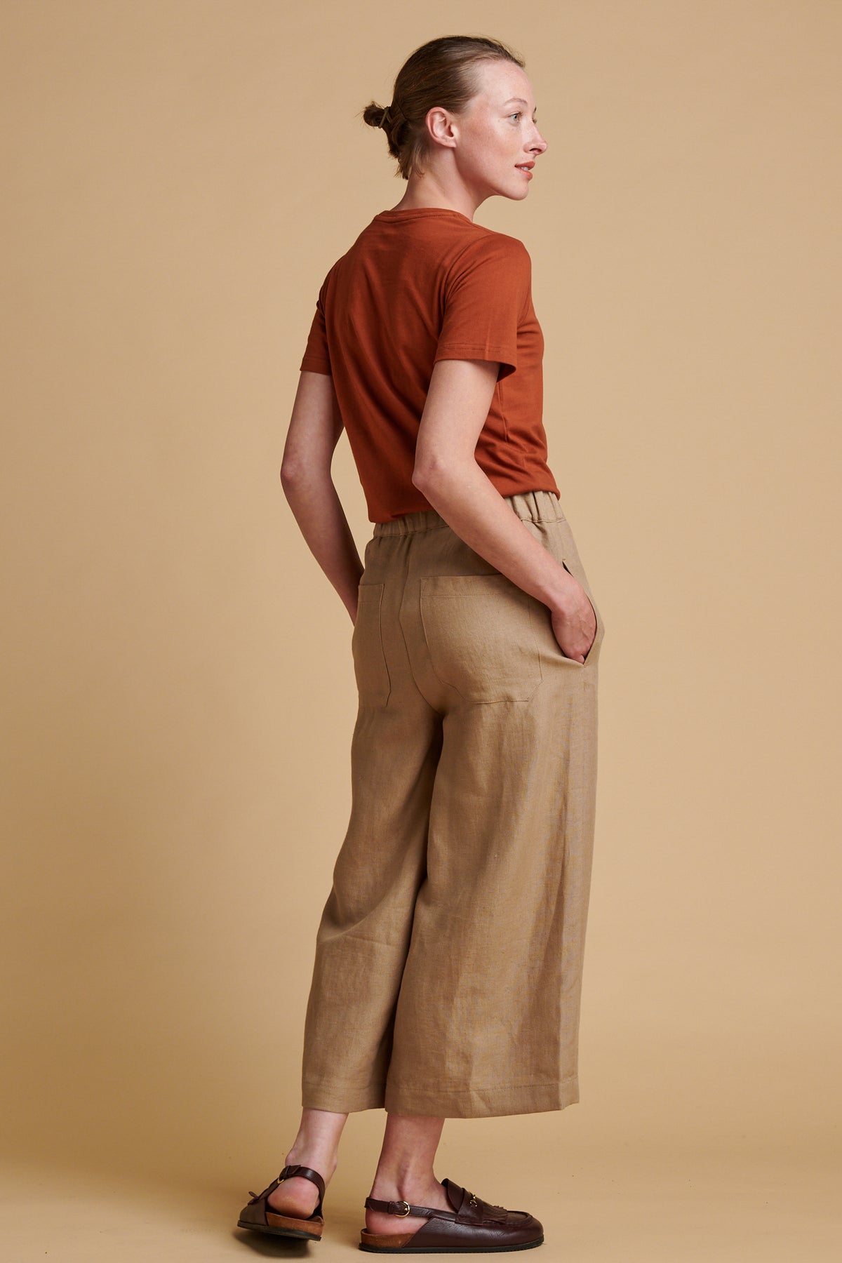 The back of female wearing short pj trousers in truffle linen paired with short sleeve crew neck t shirt in cinnamon.