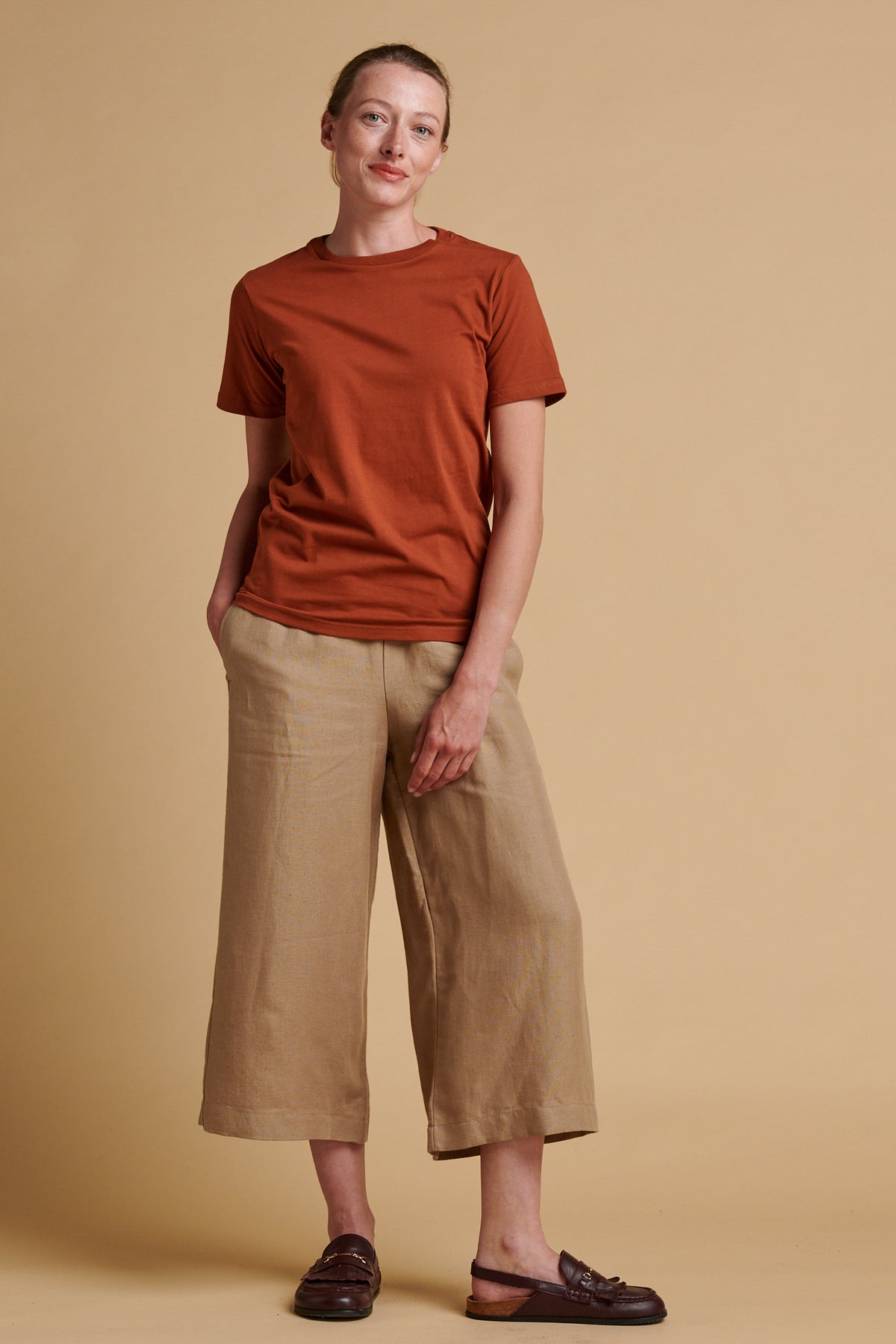 Female wearing short pj trousers in truffle linen paired with short sleeve crew neck t shirt in cinnamon.