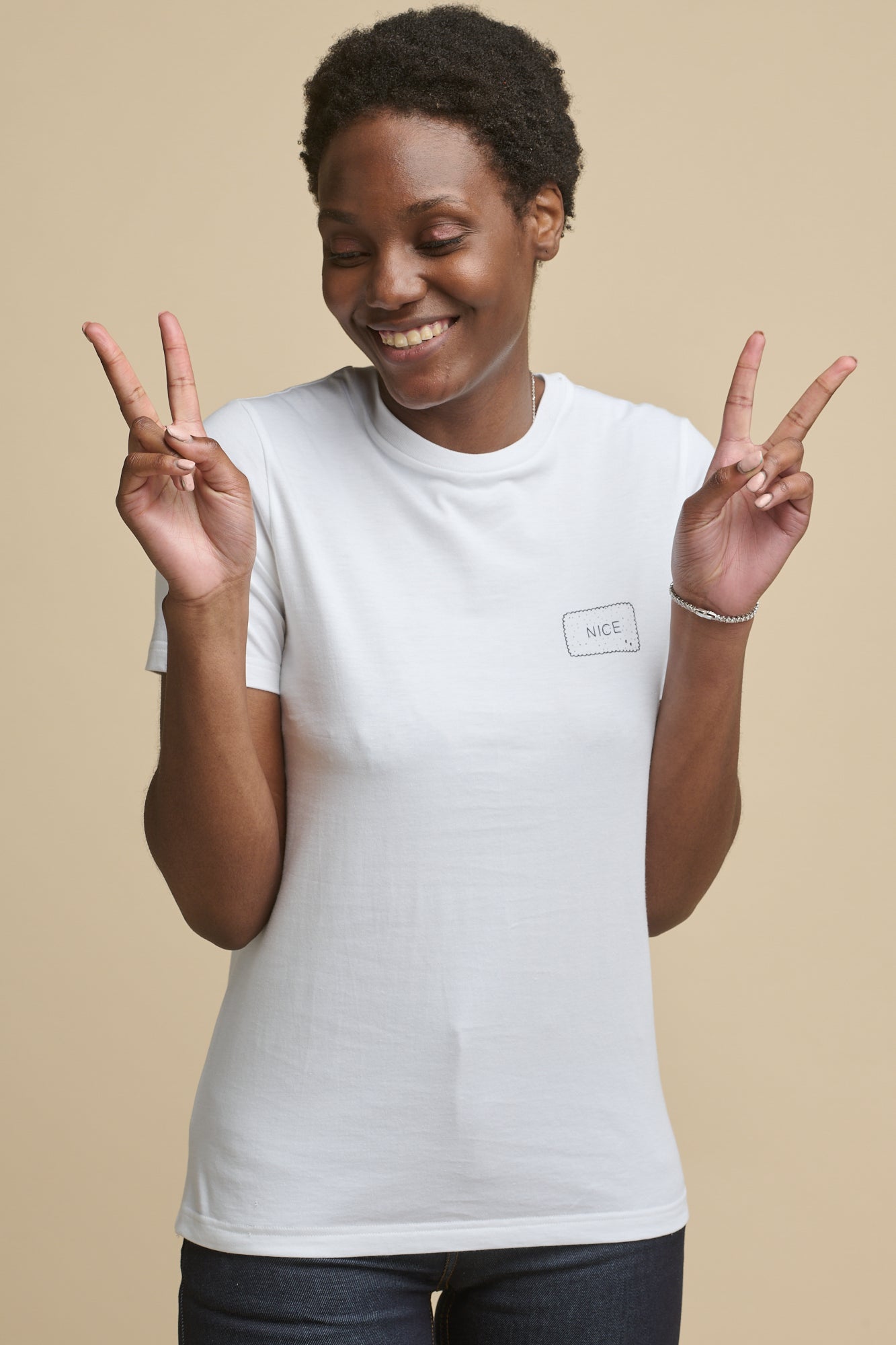 Thigh up image of the front of female wearing short sleeve graphic t shirt in white with 'Nice' print on the chest