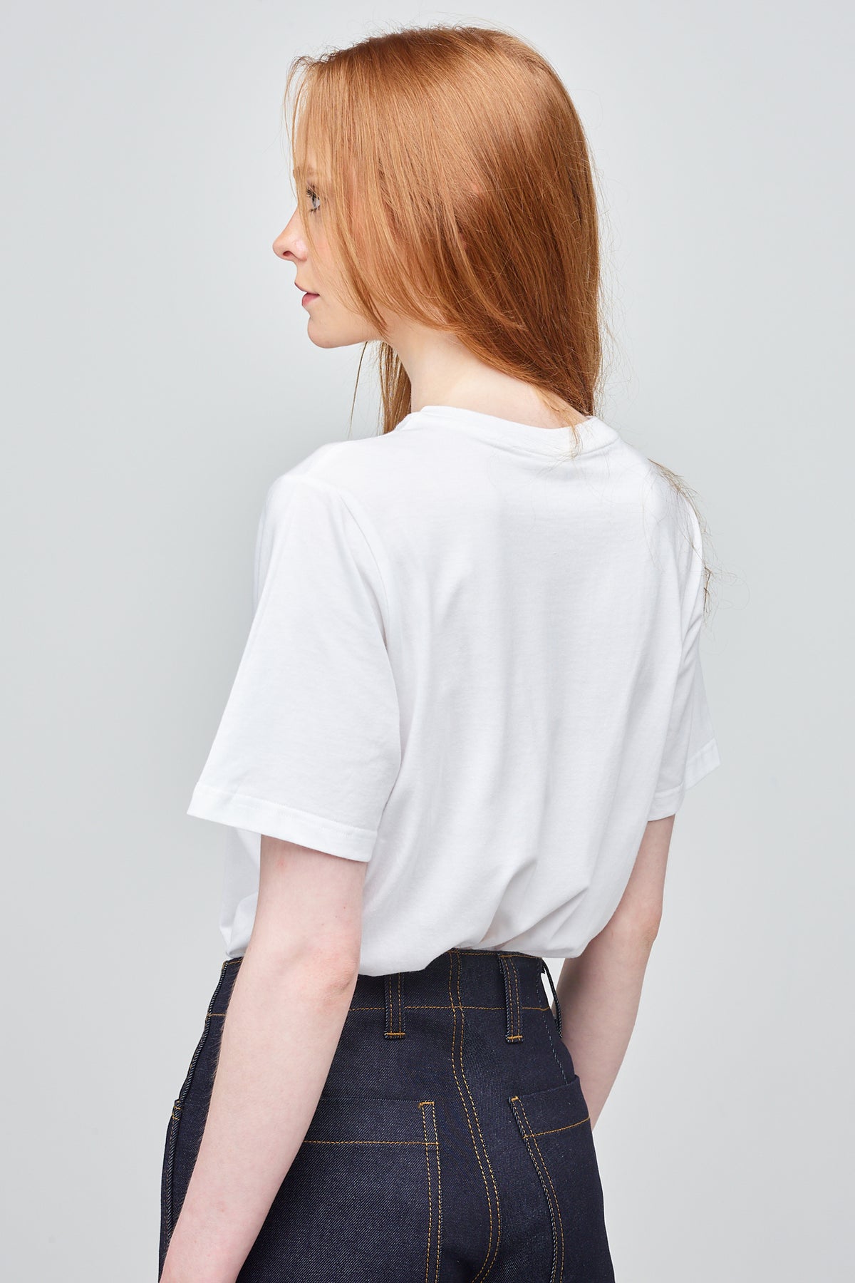 Thigh up of female from the back with ginger hair wearing white t shirt paired with indigo jean