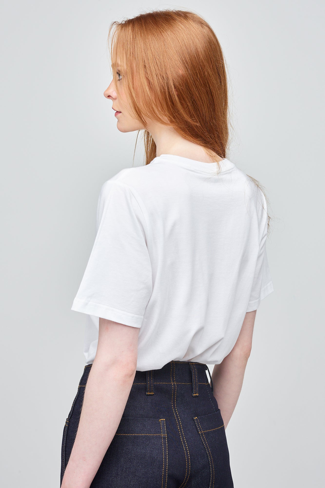 Thigh up of female with ginger hair wearing white t shirt with black Community logo on chest