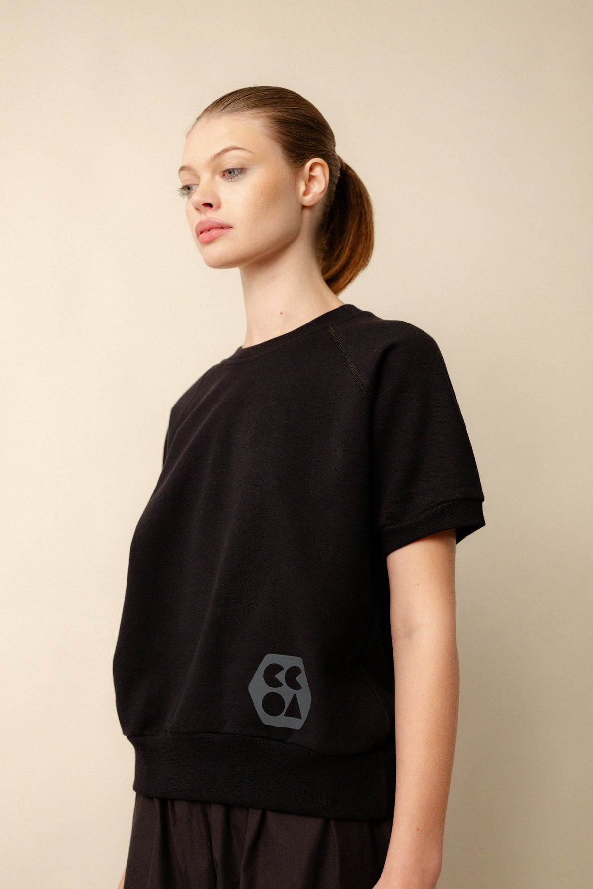 female wearing short sleeve raglan training top plastic free in black with CCOA logo at hem