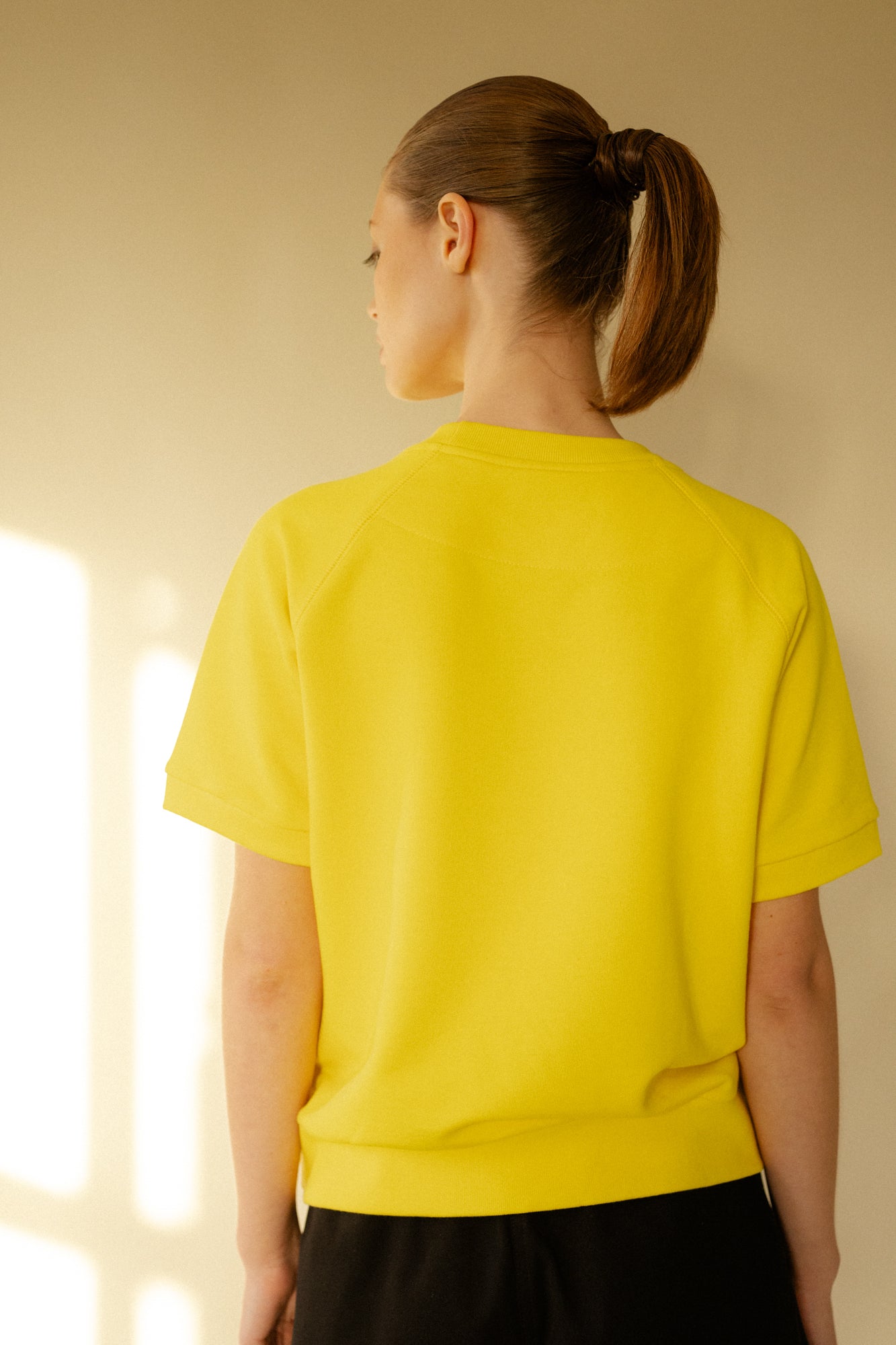 Back of white female wearing short sleeve raglan training top in Canary Yellow.