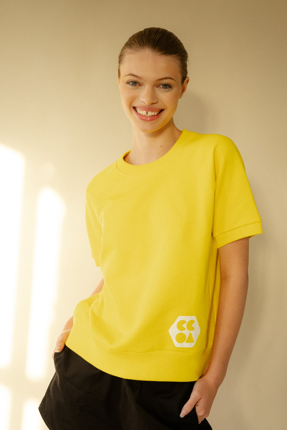 
            Smiley, white female wearing short sleeve raglan training top in Canary Yellow with white CCOA Logo.