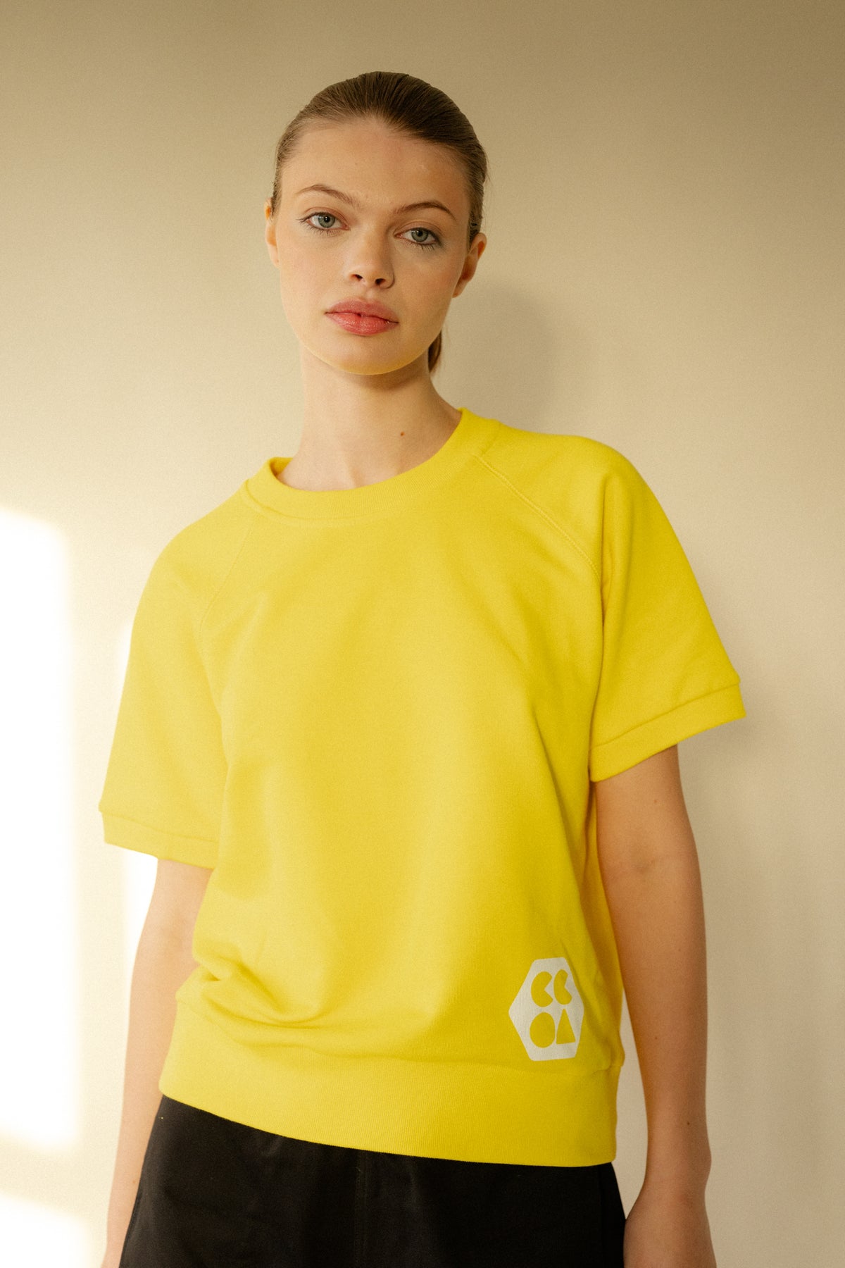 
            White female wearing short sleeve raglan training top in Canary Yellow with white CCOA Logo.