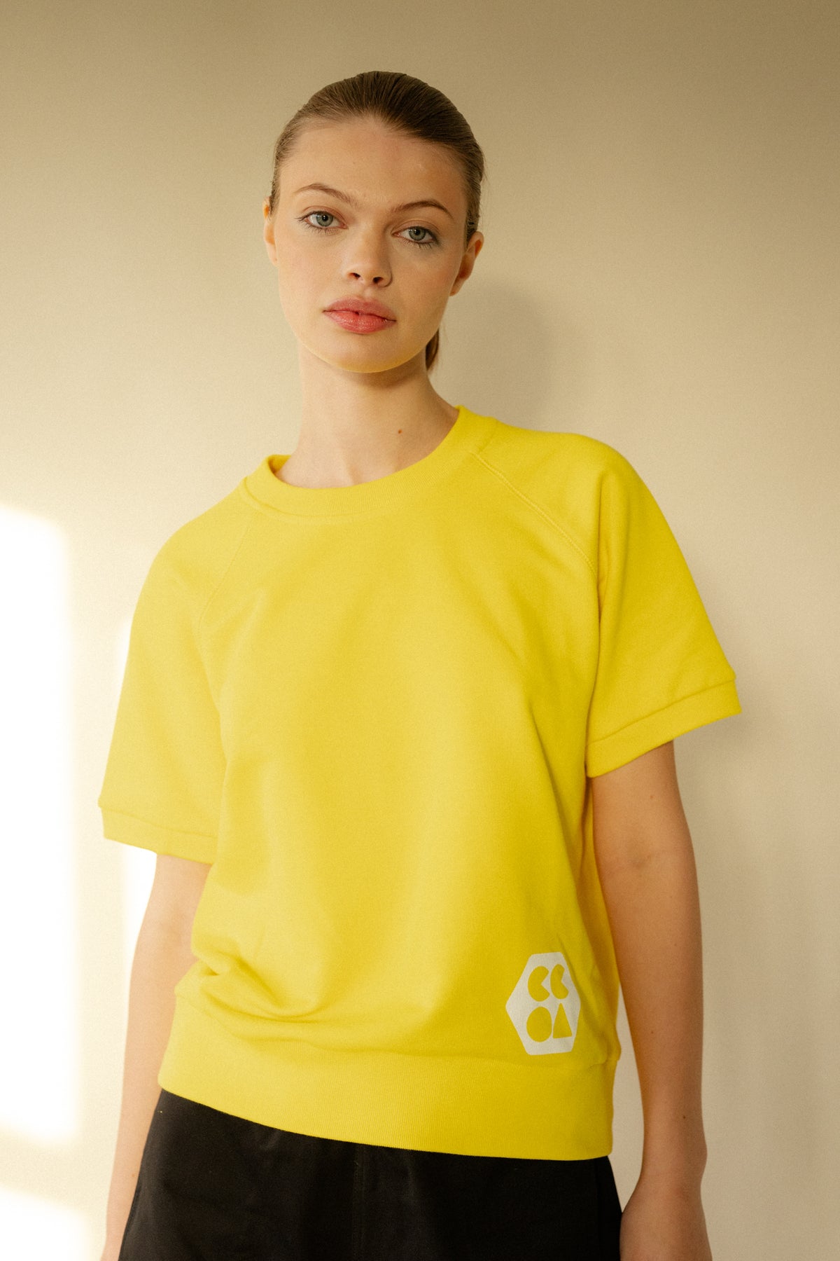 White female wearing short sleeve raglan training top in Canary Yellow with white CCOA Logo.