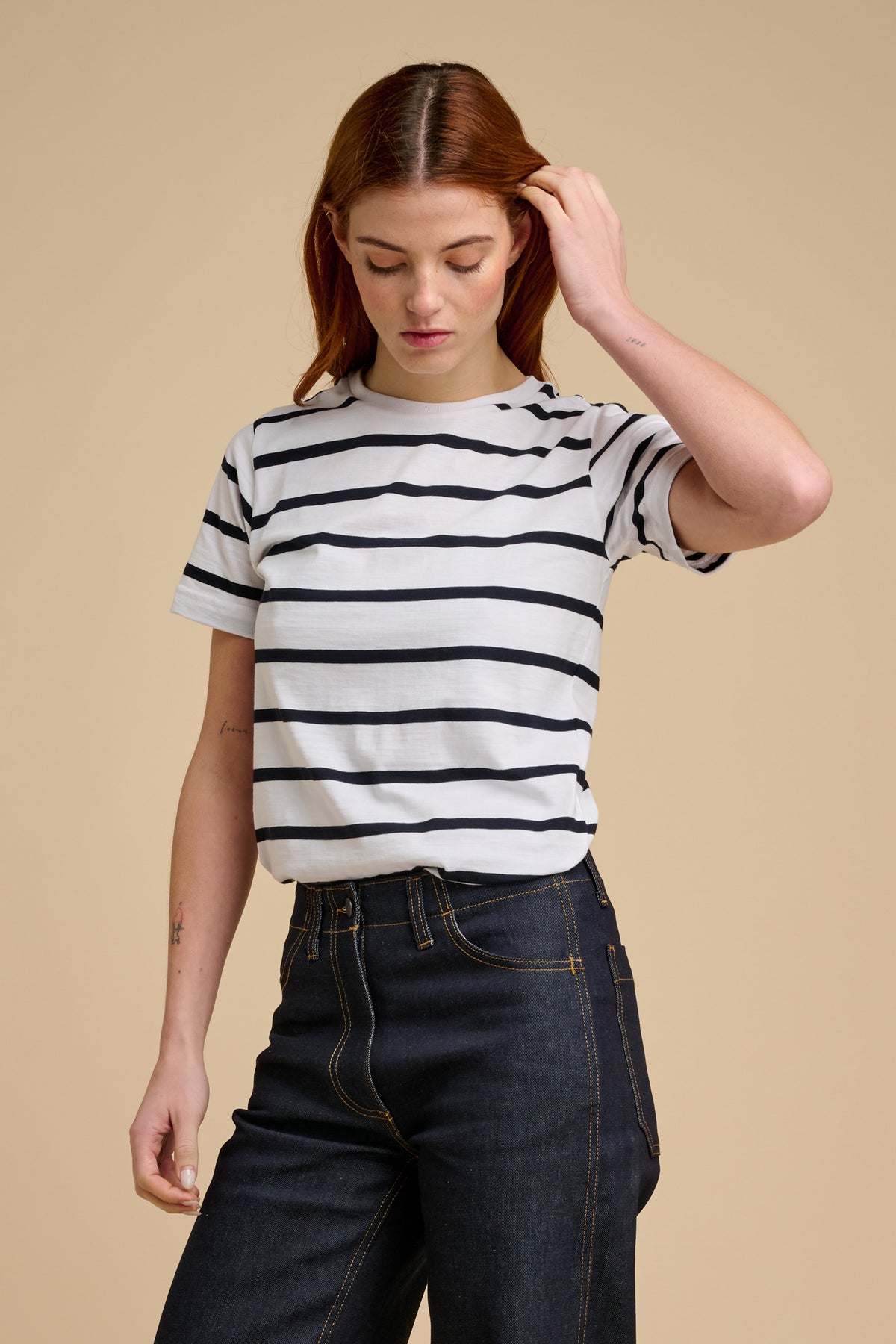 Woman wearing a navy and white striped shirt and dark jeans on a beige background