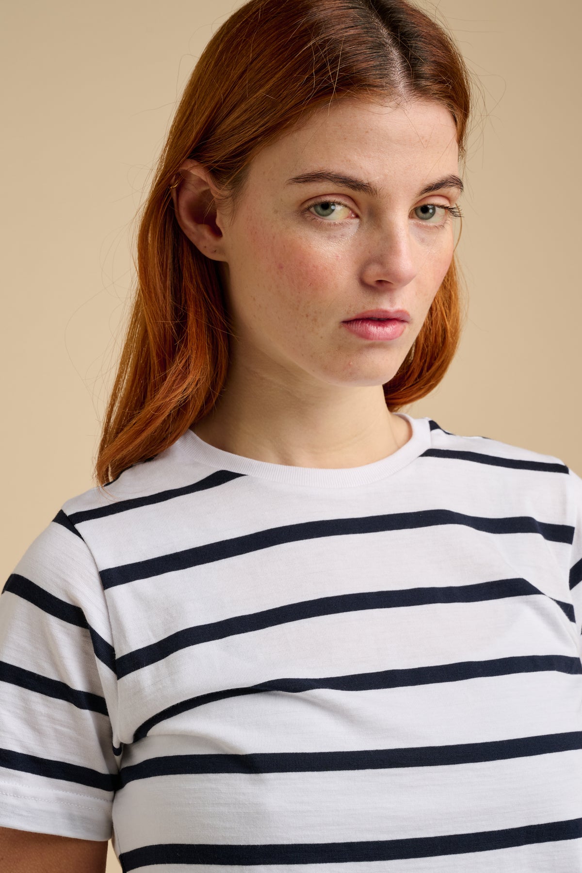 Woman wearing a white and navy striped shirt against a beige background