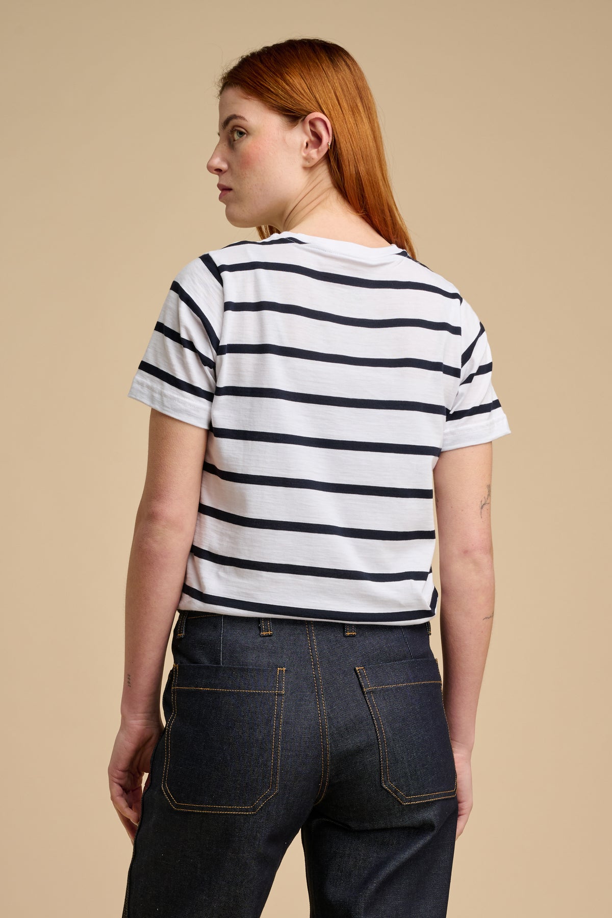The back of woman wearing a navy and white striped shirt and dark jeans on a beige background