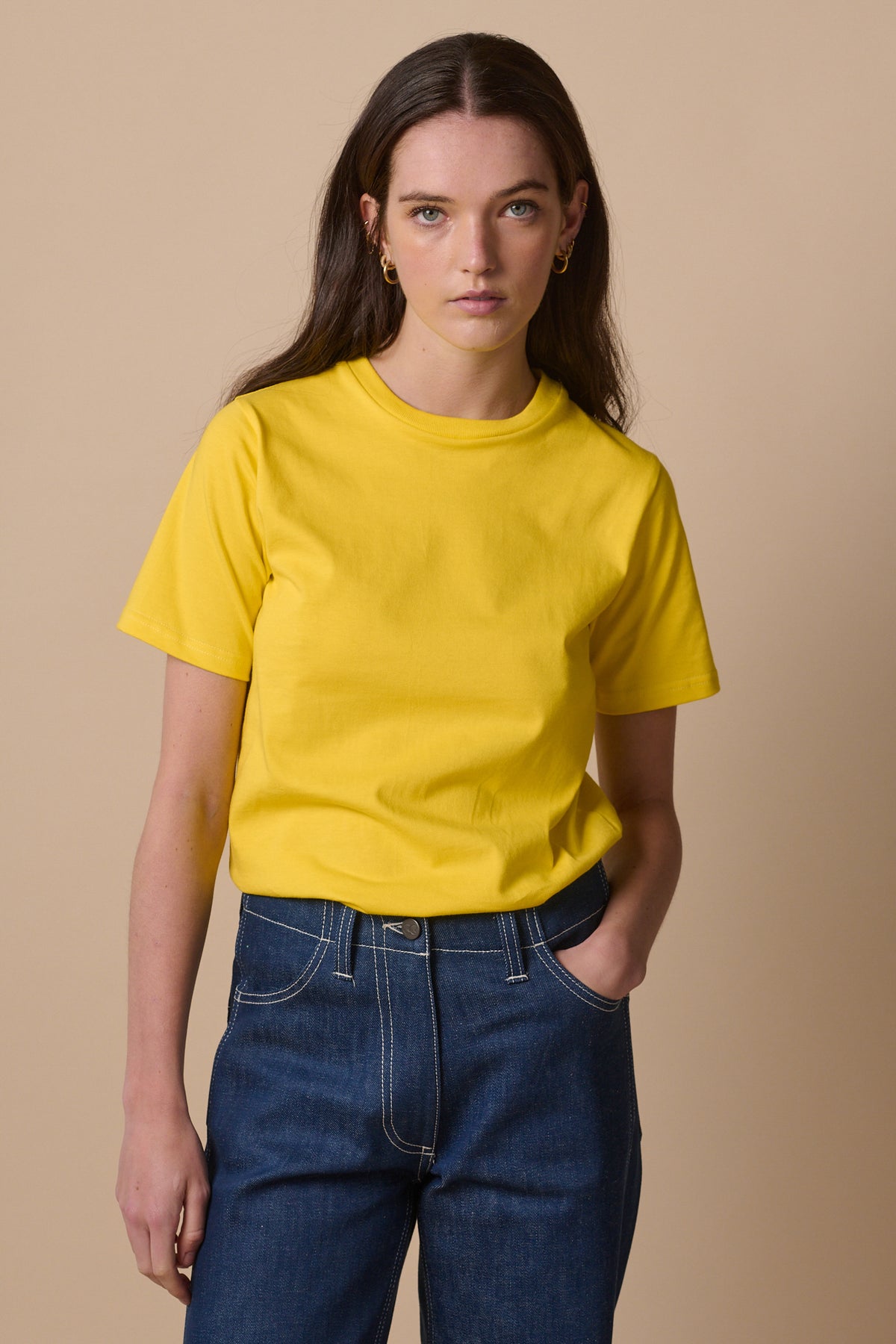White female wearing short sleeve crew neck t shirt in canary yellow tucked into blue jeans